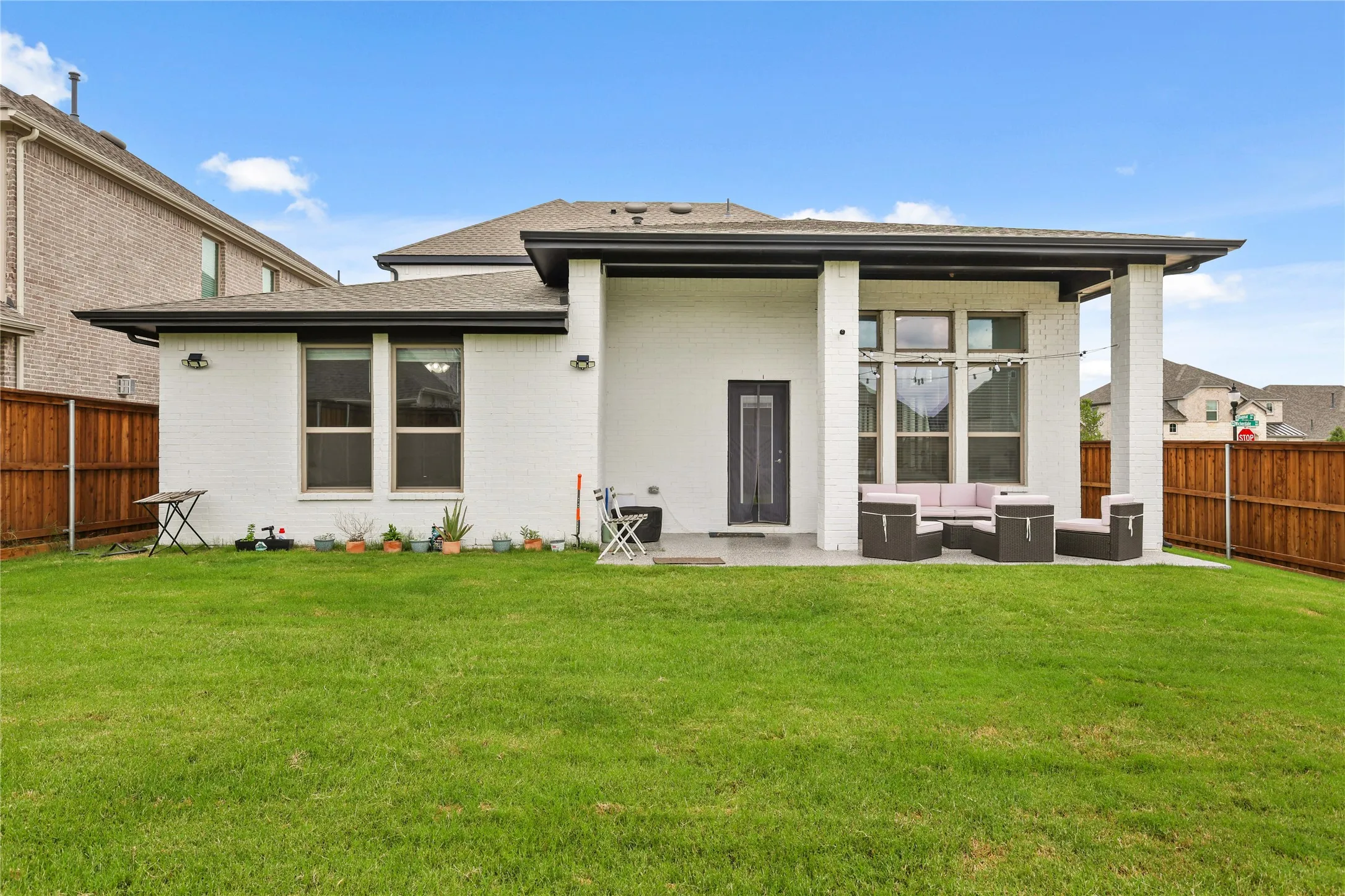 Expansive backyard featuring a manicured lawn, a covered patio, white brick exterior, dark trim, and a privacy fence