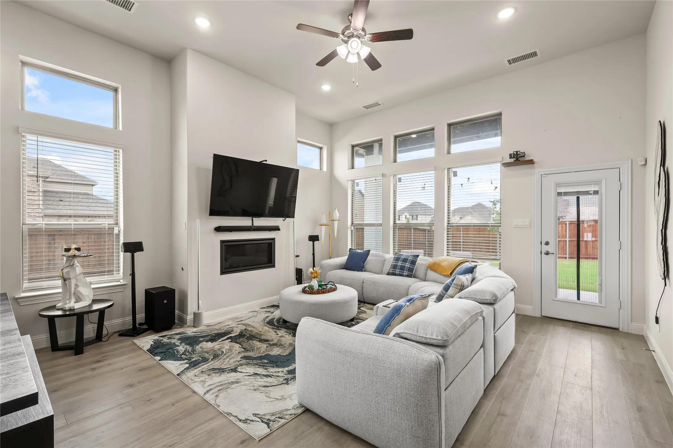 Vaulted ceiling living area featuring wood-finish flooring and multiple windows with blinds