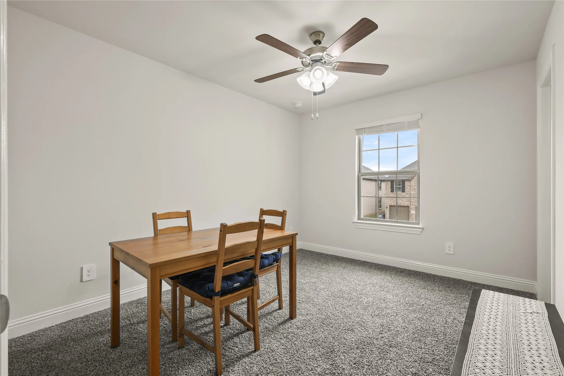 Recessed window with a white frame and blinds, light gray wall paint, gray textured carpet, white baseboards, and a ceiling fan with light fixture