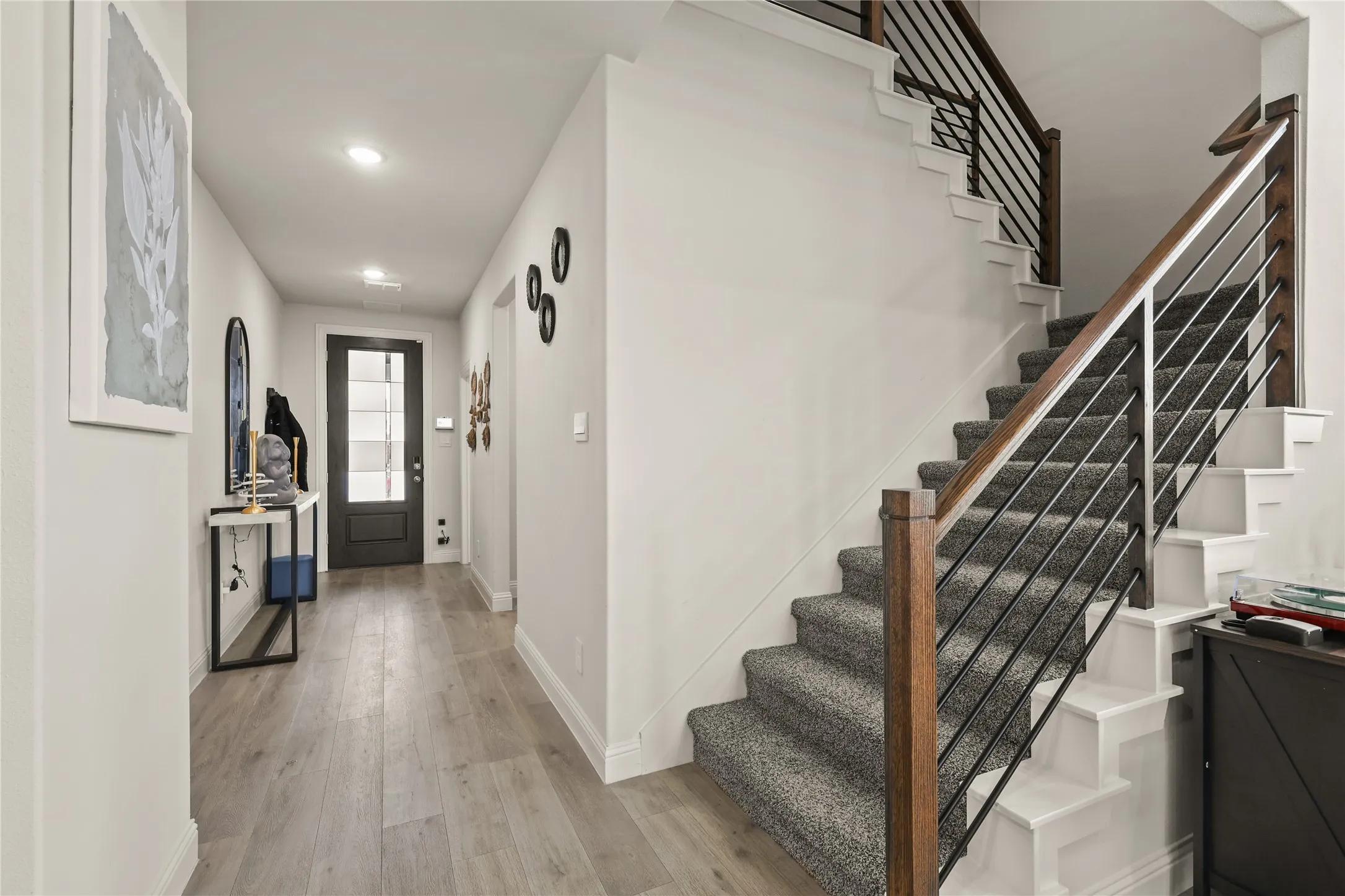 Entryway featuring wood-finish flooring, a contemporary staircase with dark wood handrails and black metal balusters, recessed lighting, and a dark paneled door with glass inserts