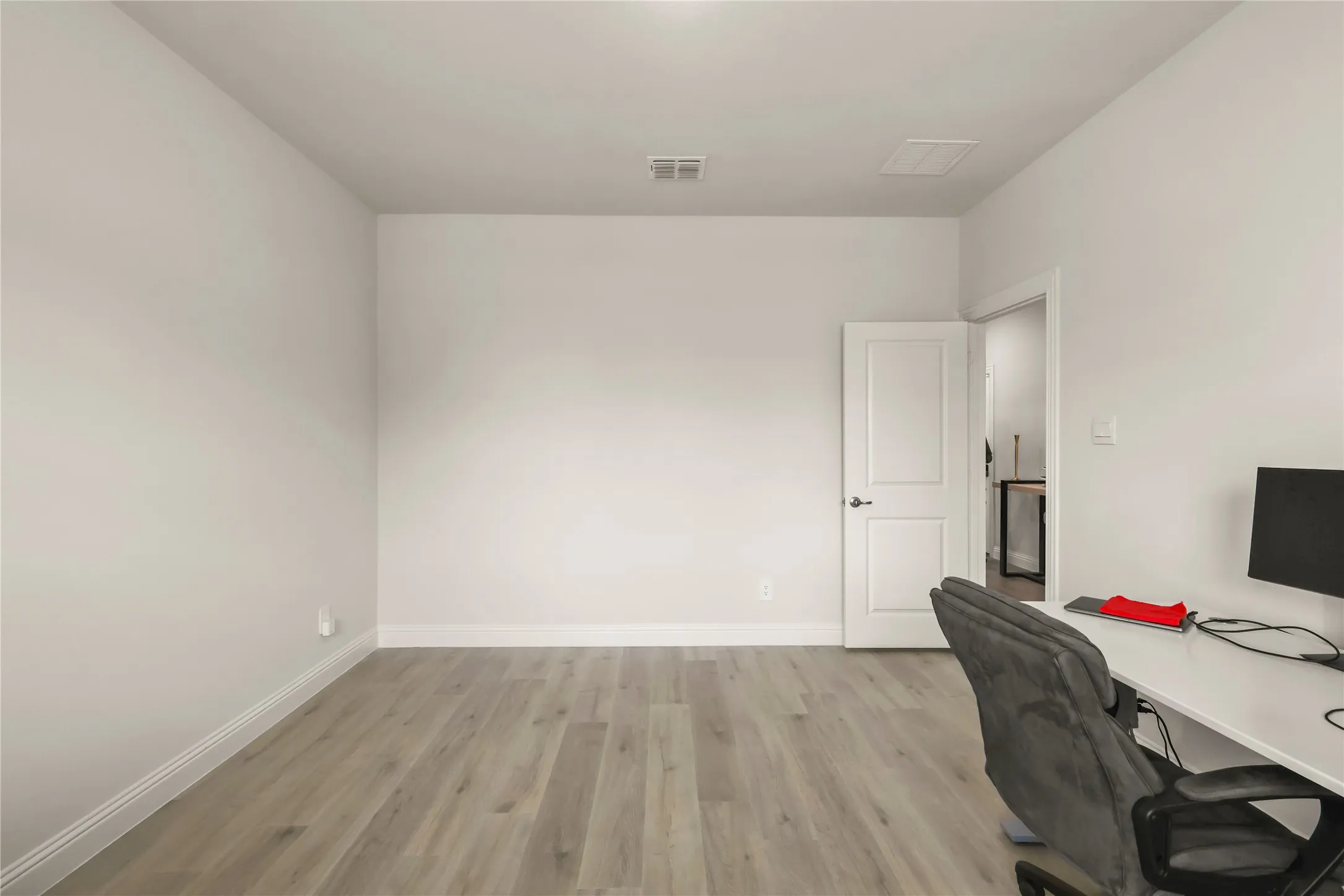 Bright room featuring wood-finish flooring, white baseboards, and a white paneled door with dark hardware