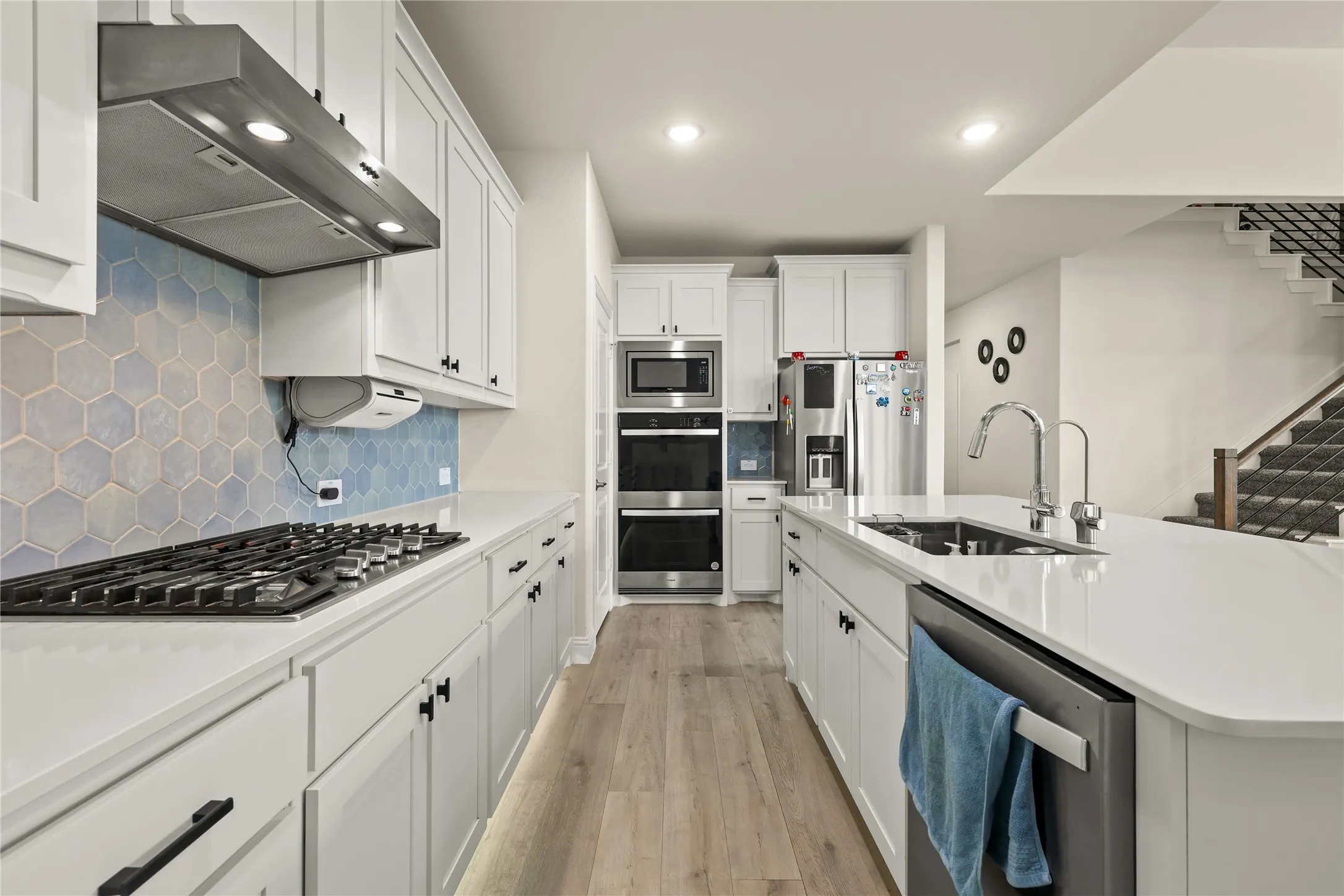 Modern kitchen featuring white cabinetry, light countertops, wood-finish flooring, a hexagon tile backsplash, and stainless steel appliances