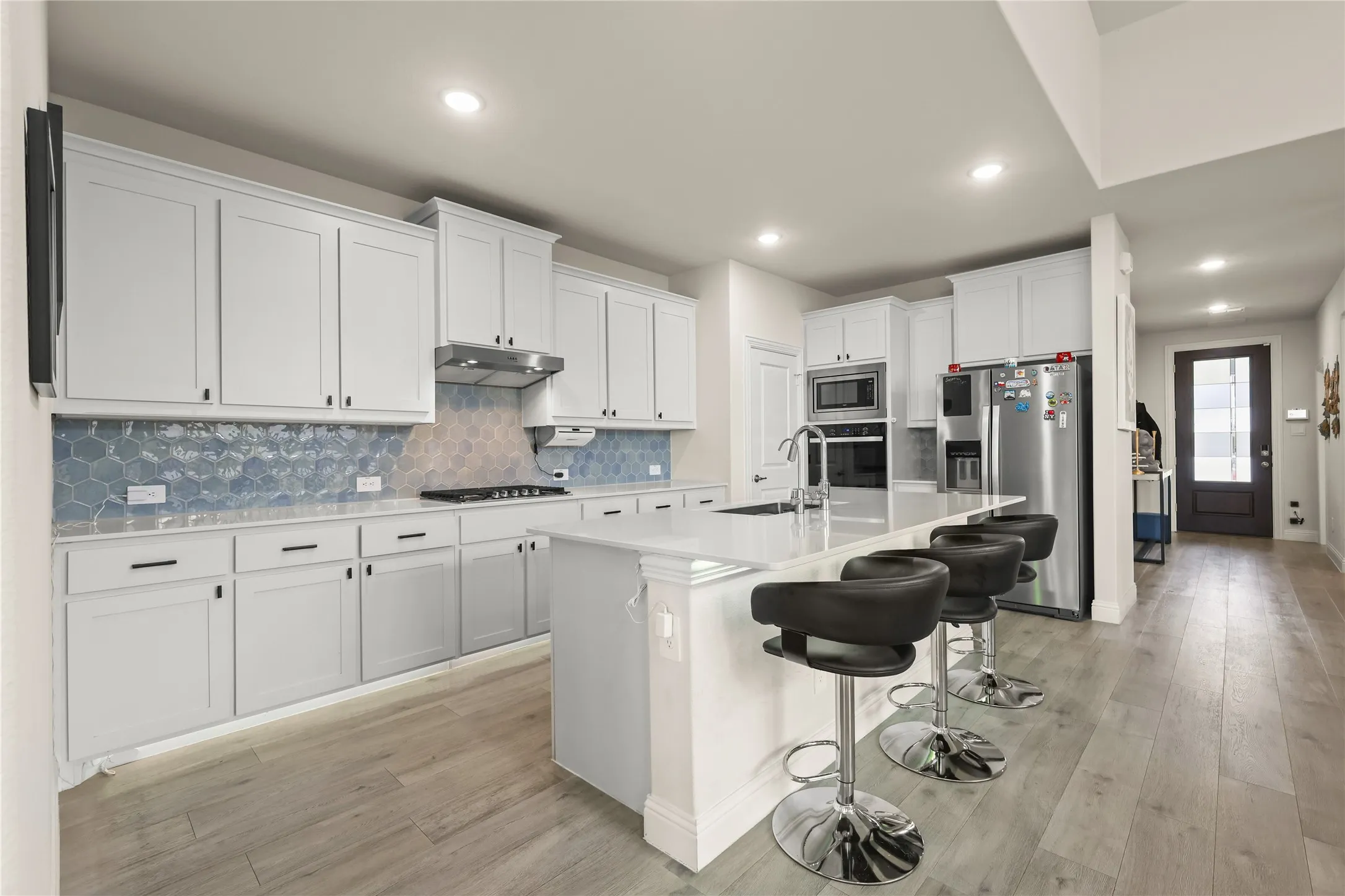 Modern kitchen featuring white cabinetry, a large kitchen island with seating, integrated stainless steel appliances, a gas cooktop, and a distinctive blue hexagonal tile backsplash
