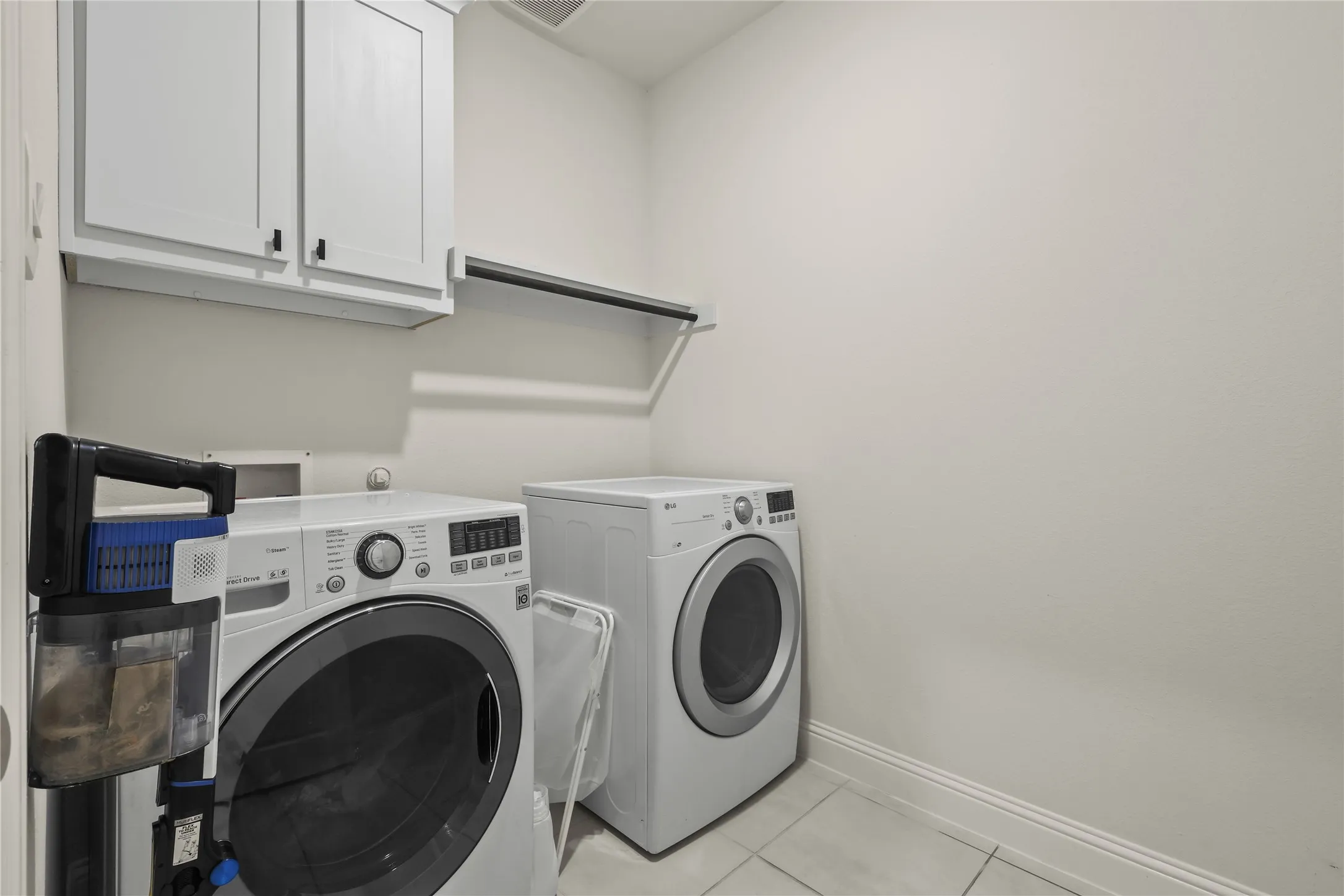 Laundry area featuring white cabinetry with black hardware, a built-in hanging rod, and light tile flooring
