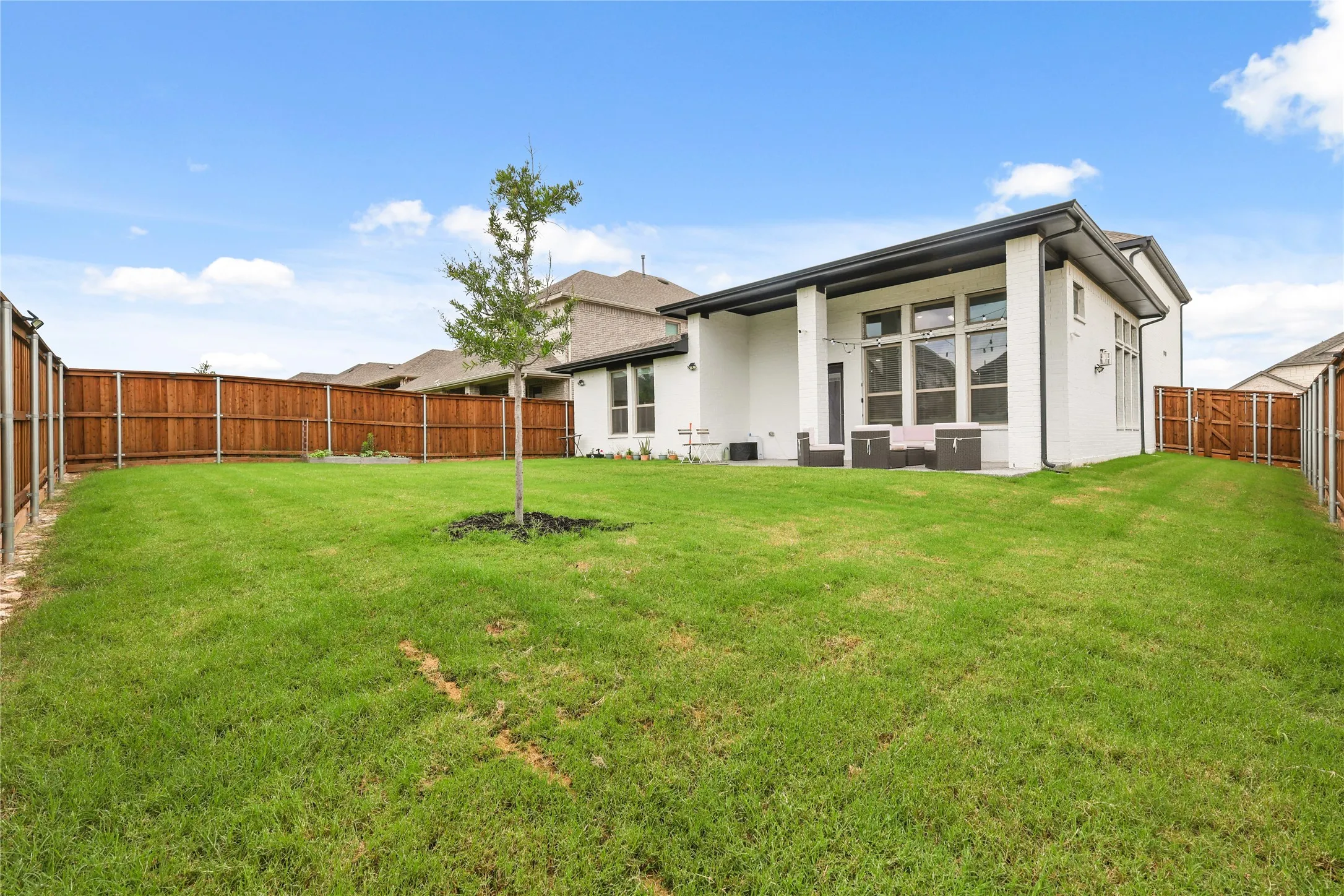 Expansive backyard featuring a manicured lawn, a young tree, and a full wood privacy fence