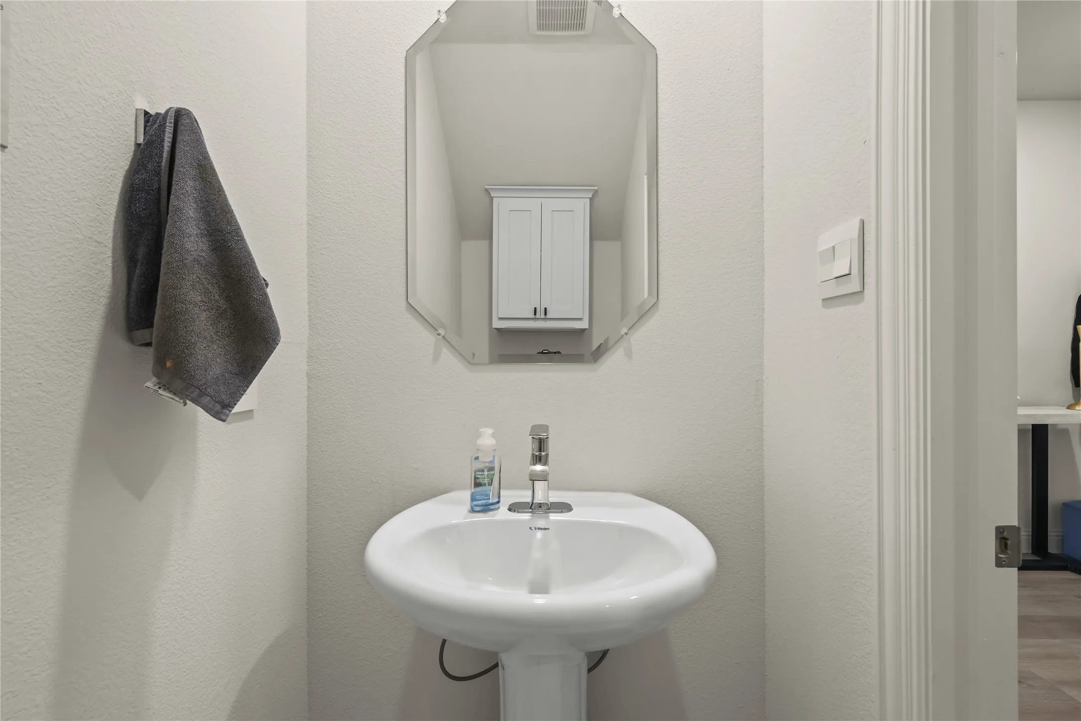 Pedestal sink with a polished chrome faucet, complemented by an octagonal wall-mounted mirror