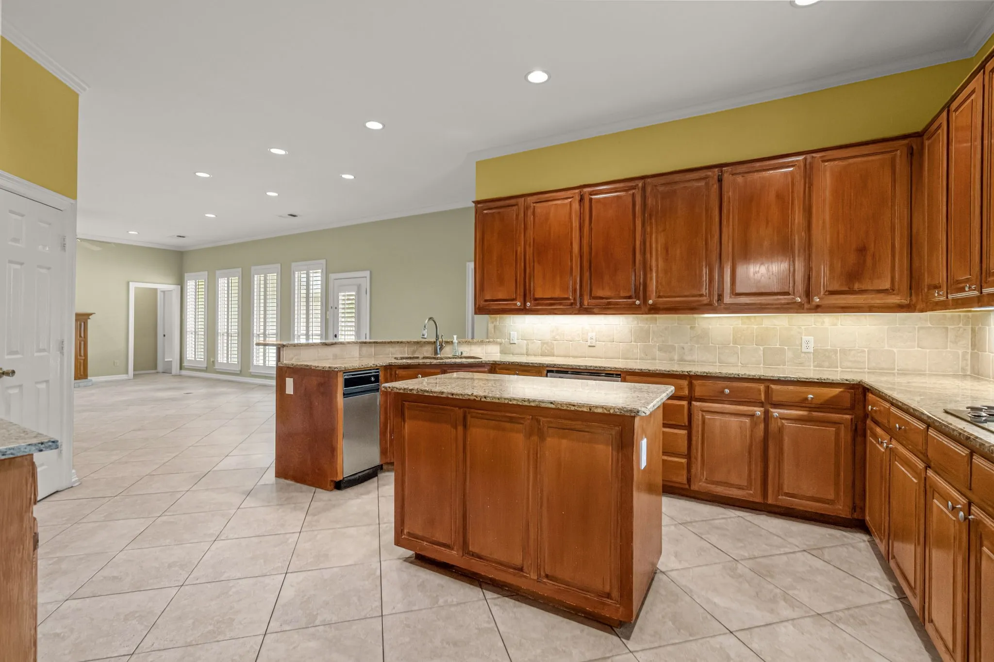 Spacious kitchen featuring a central island, wood cabinetry, stone-finish countertops, and a tile backsplash
