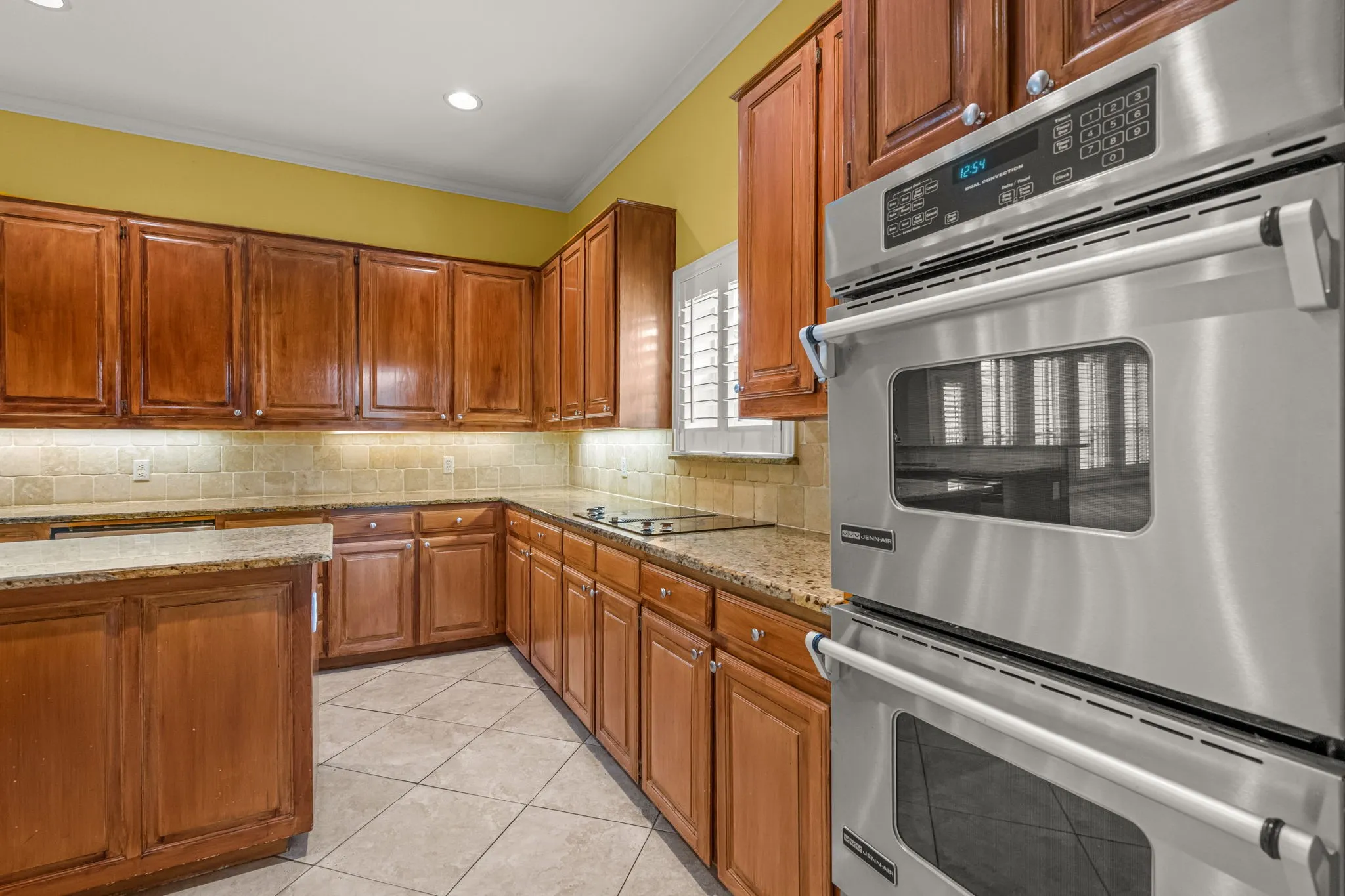 Kitchen featuring wood-finish cabinetry, granite-style countertops, mosaic tile backsplash, and stainless steel double ovens