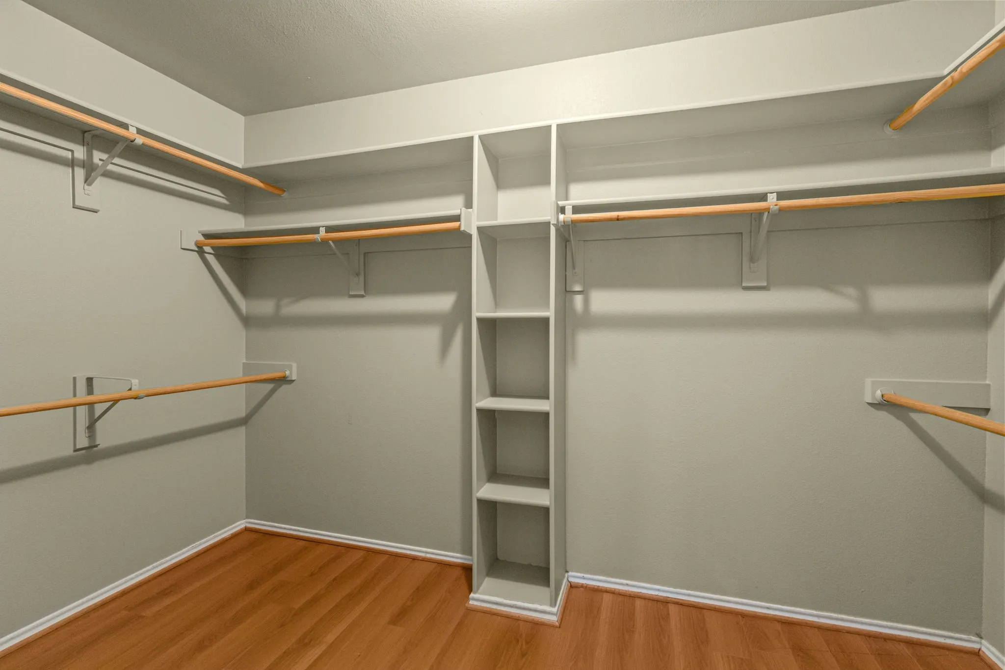 Custom closet system featuring built-in shelving, multiple hanging rods, and wood-finish flooring