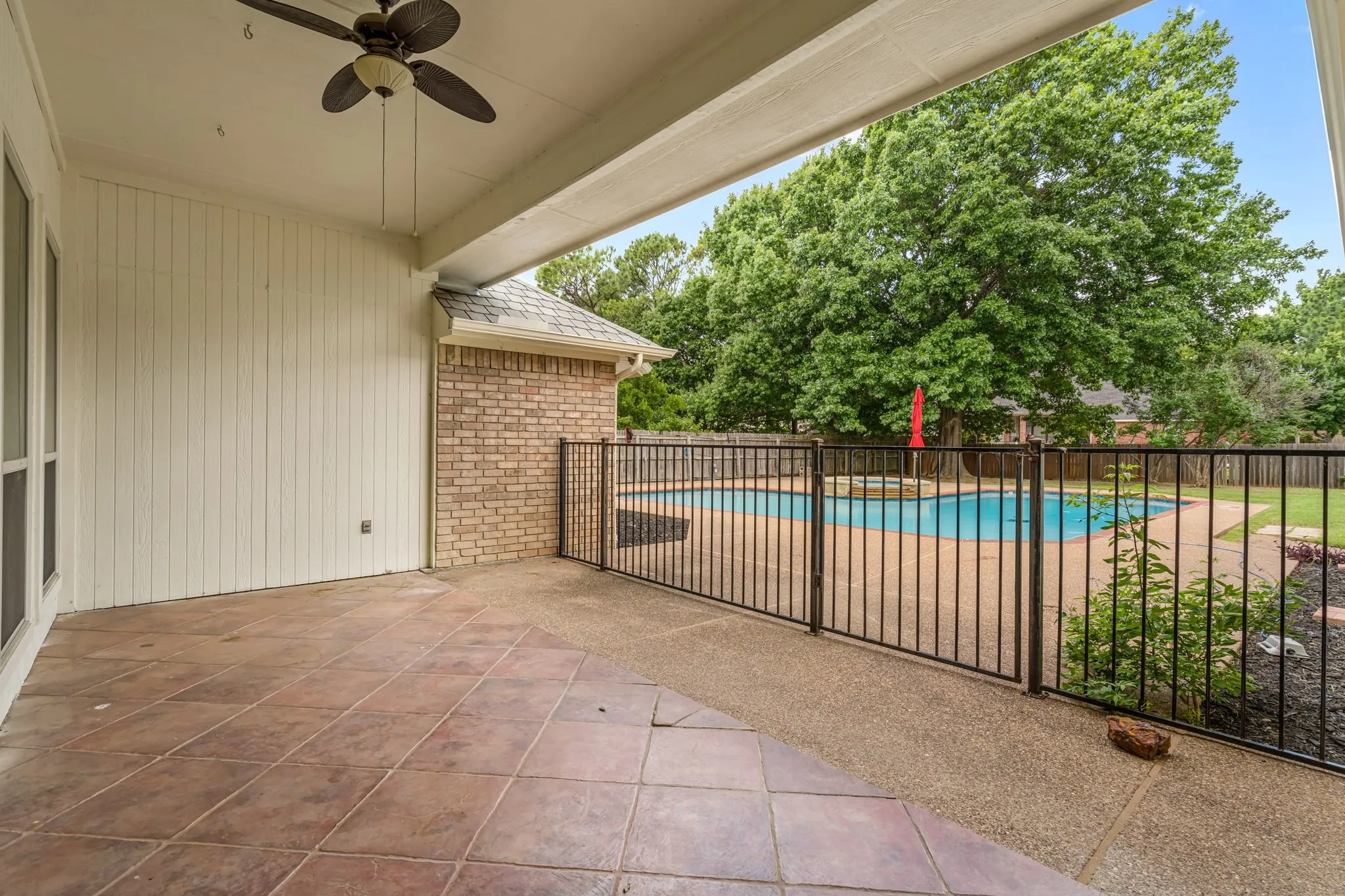 Covered patio featuring a ceiling fan, tile flooring, and direct access to the fenced pool area