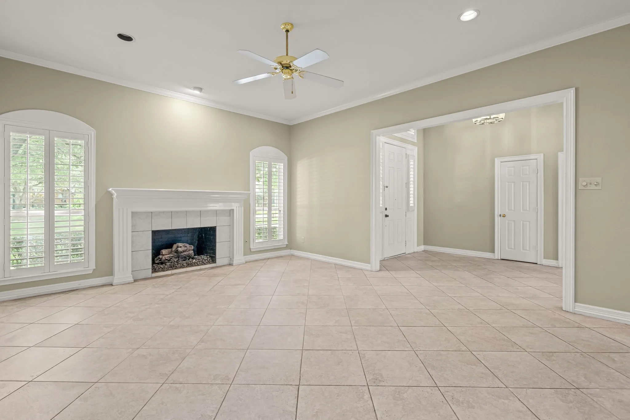 Spacious interior featuring neutral tile flooring, a decorative fireplace with a white mantel, and arched windows with plantation shutters