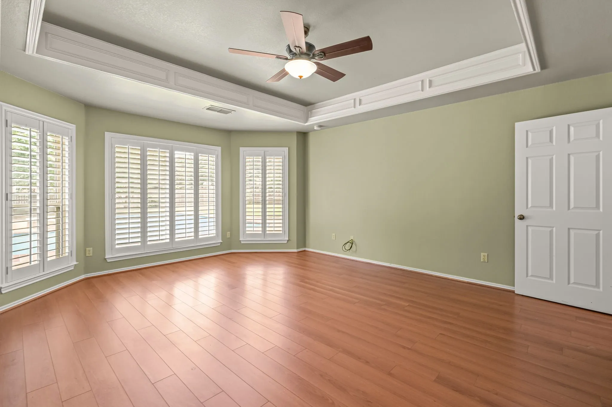 Spacious room featuring wood-finish flooring, a tray ceiling with crown molding, and a ceiling fan