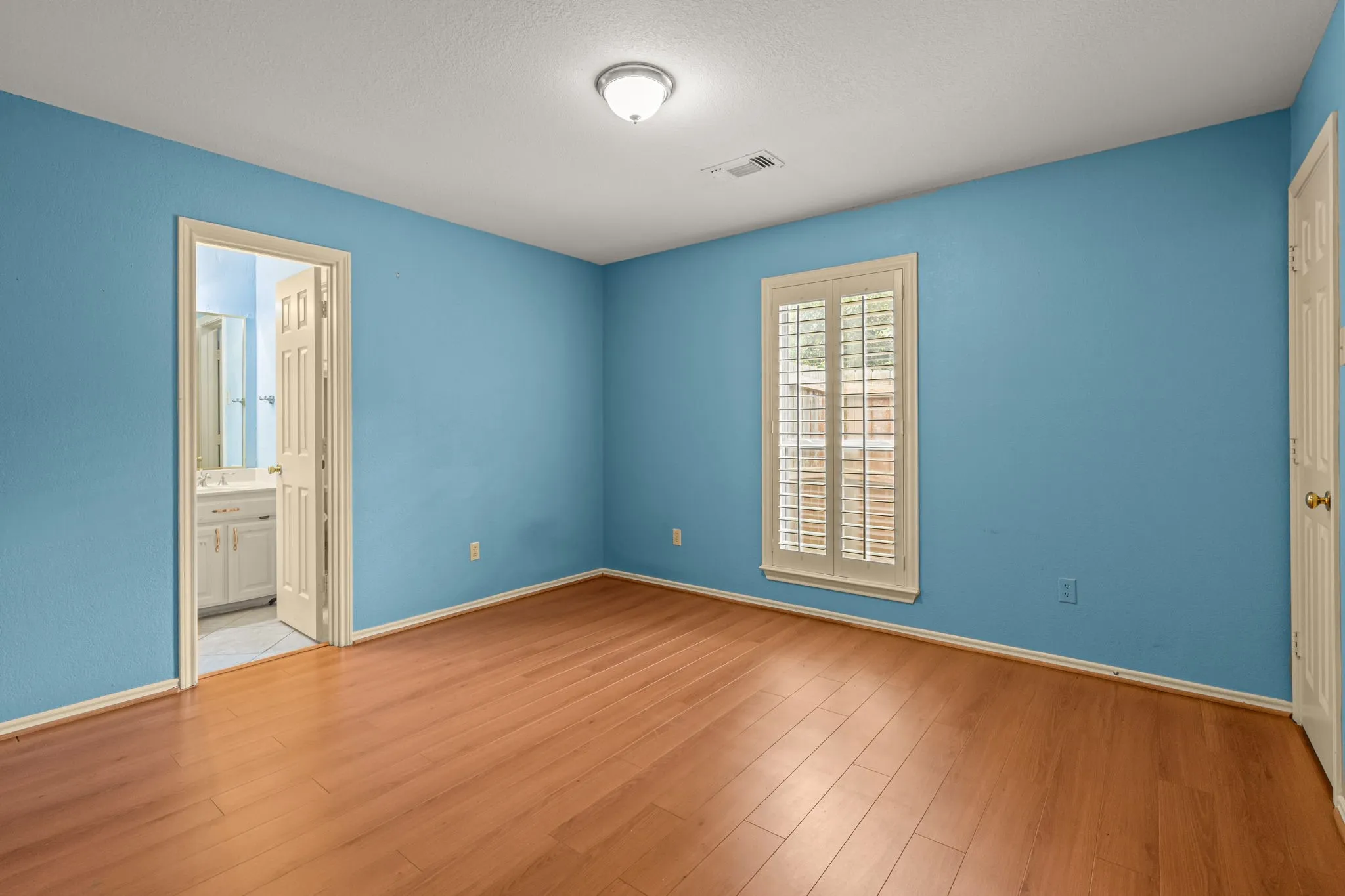 Spacious interior room featuring wood-finish flooring, a window with plantation shutters, and a ceiling-mounted light fixture