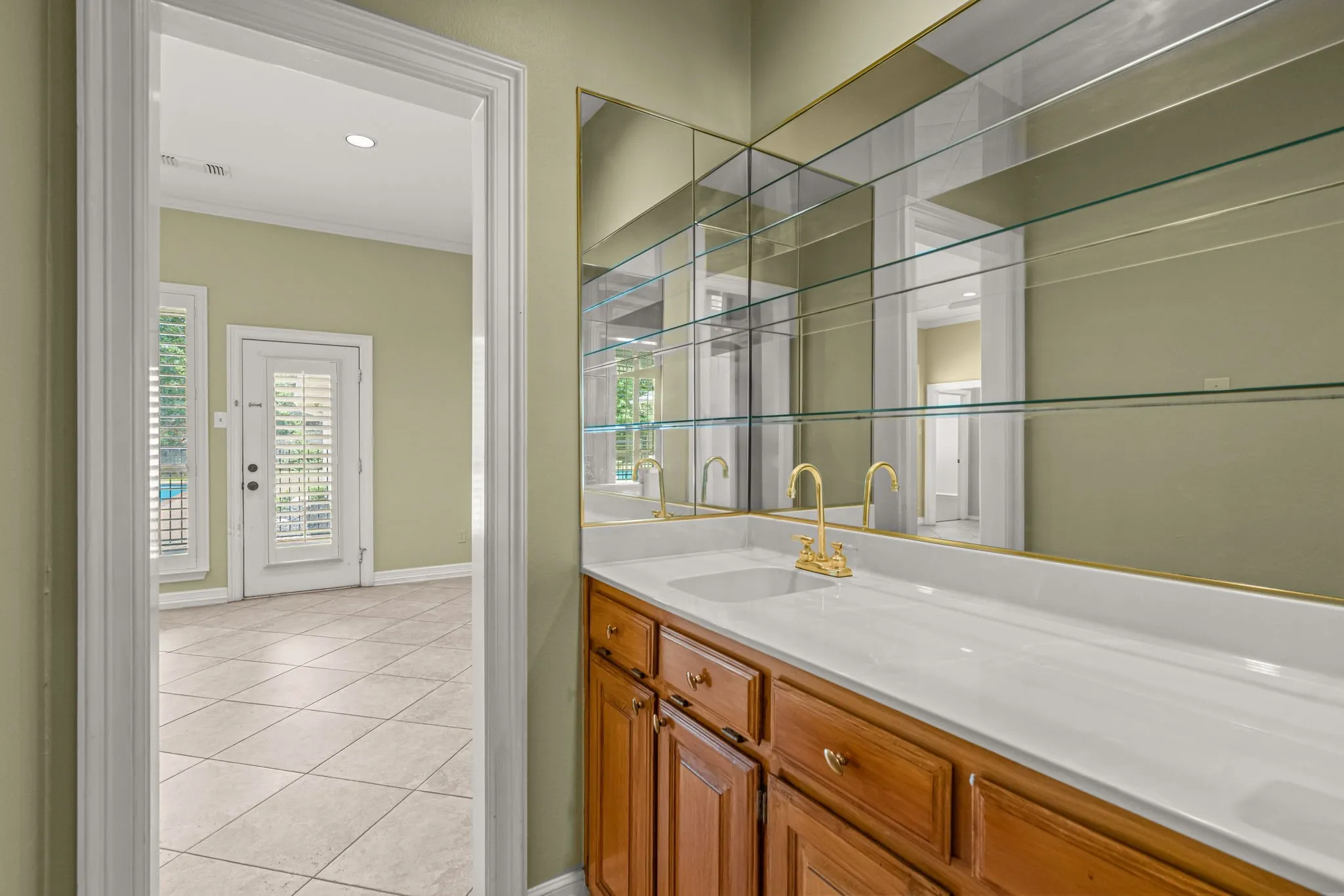 Integrated wet bar with a white countertop, dual brass-finish faucets, and an expansive mirrored backsplash with glass shelving