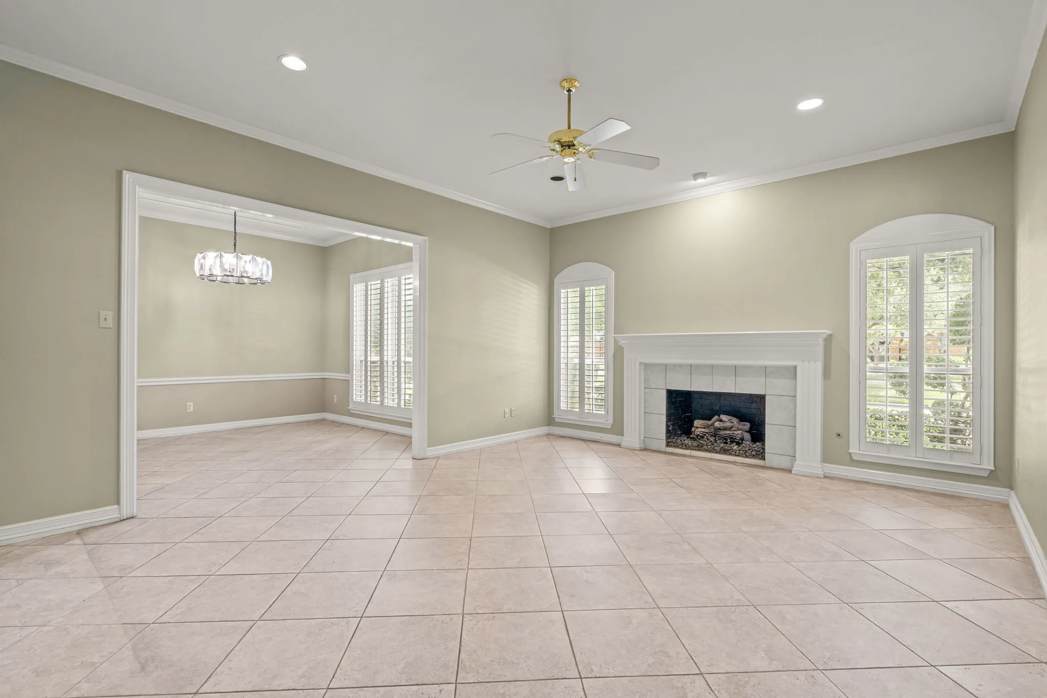 Spacious room with tile flooring, a detailed fireplace, and large arched windows featuring plantation shutters