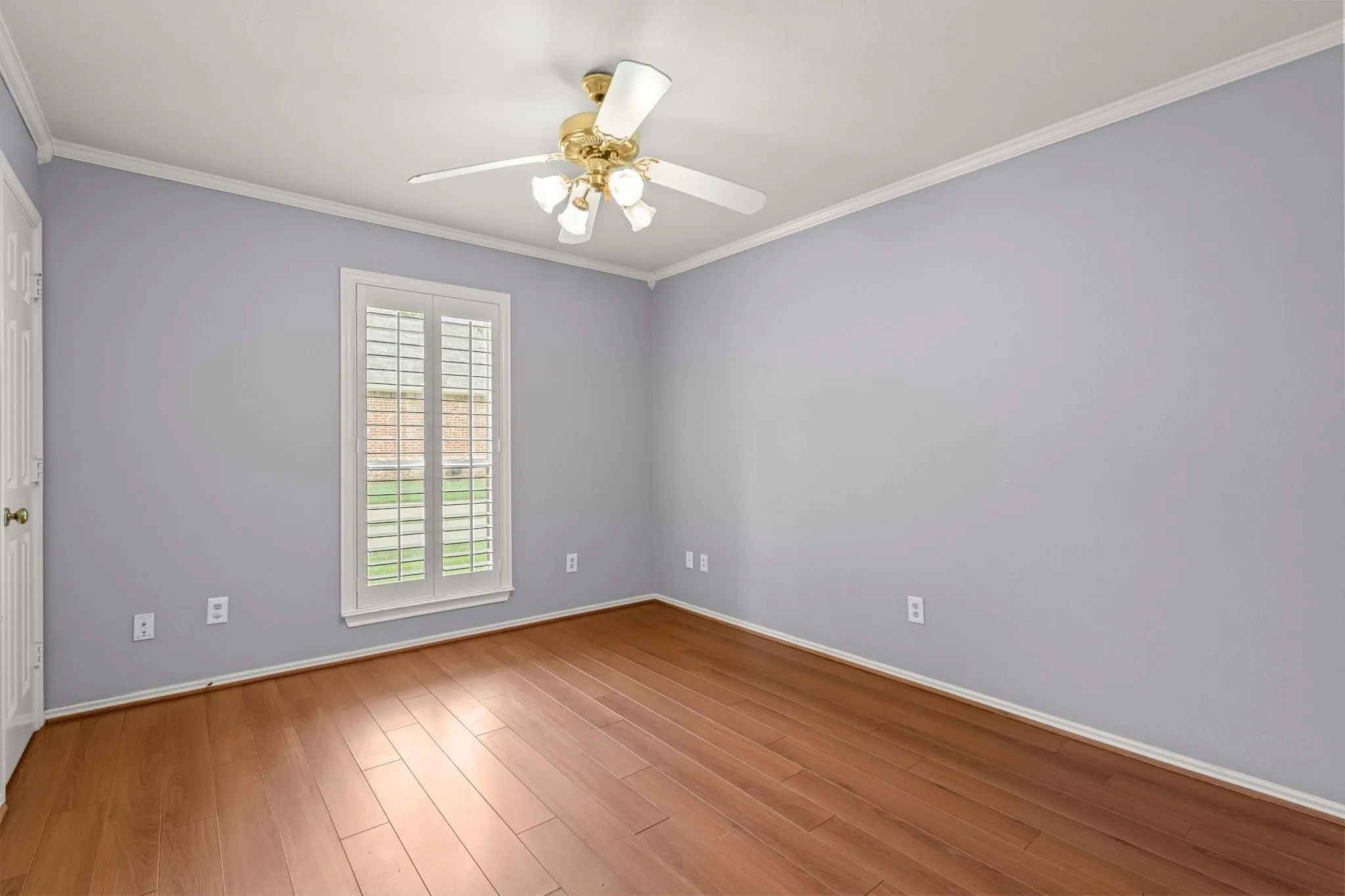 Interior space featuring wood-finish flooring, a window with plantation shutters, crown molding, and a ceiling fan with integrated lighting