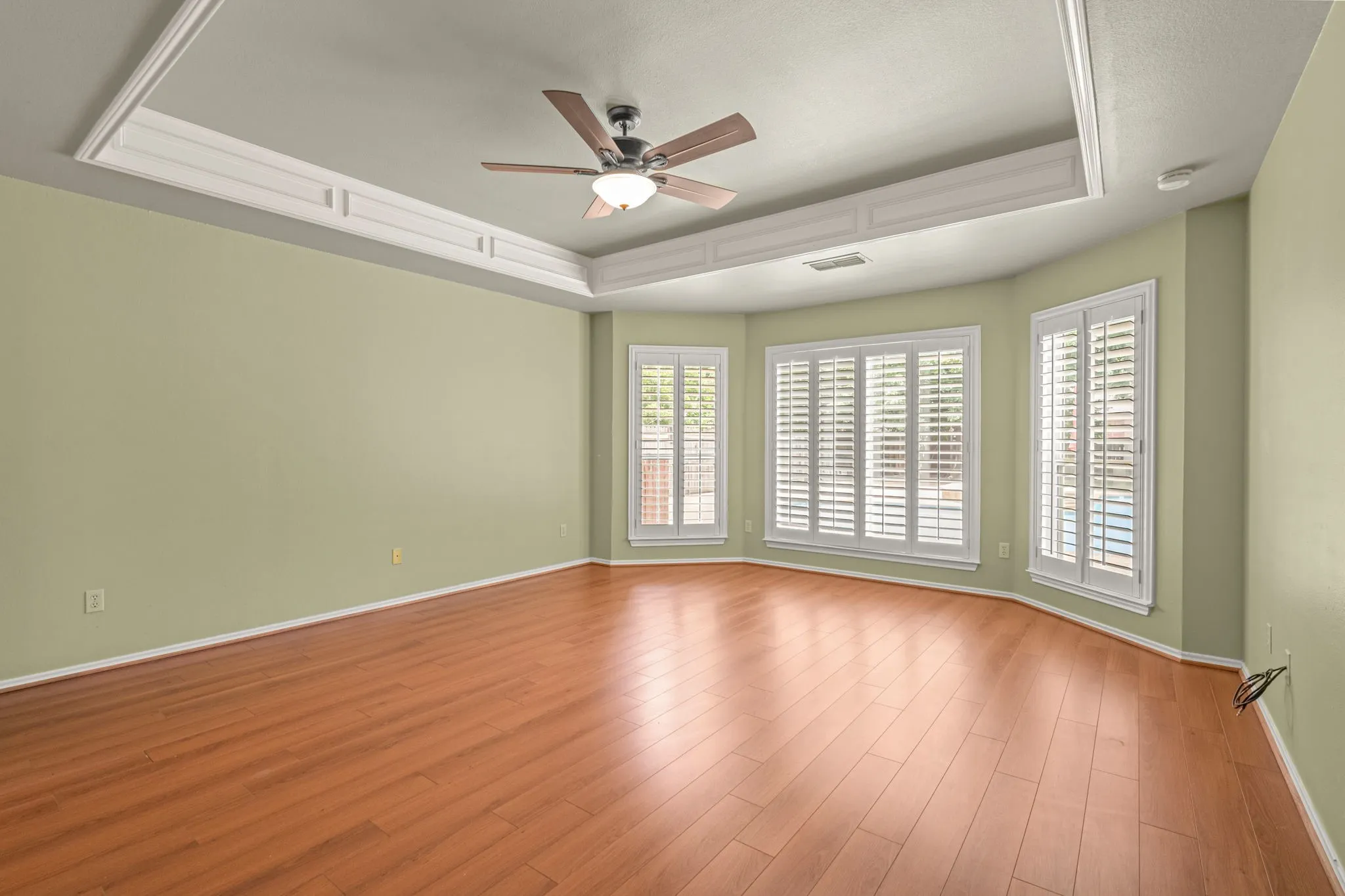 Spacious interior room featuring wood-finish flooring, a tray ceiling with crown molding, and a ceiling fan with integrated lighting