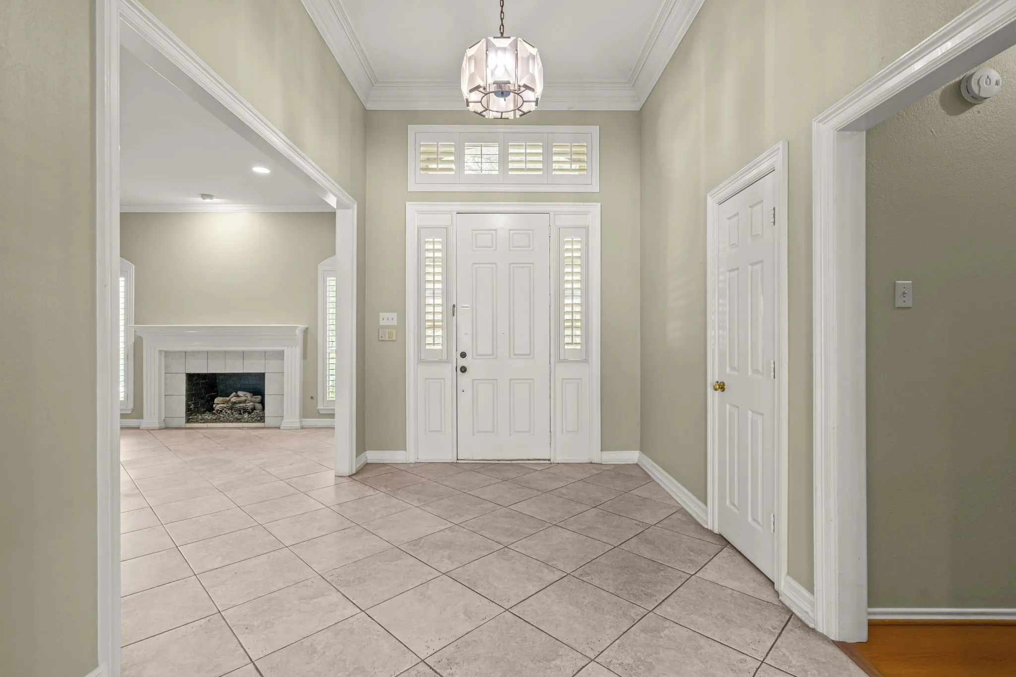 Entry foyer featuring ceramic tile flooring, a decorative chandelier, and a white paneled door with sidelights and a transom window
