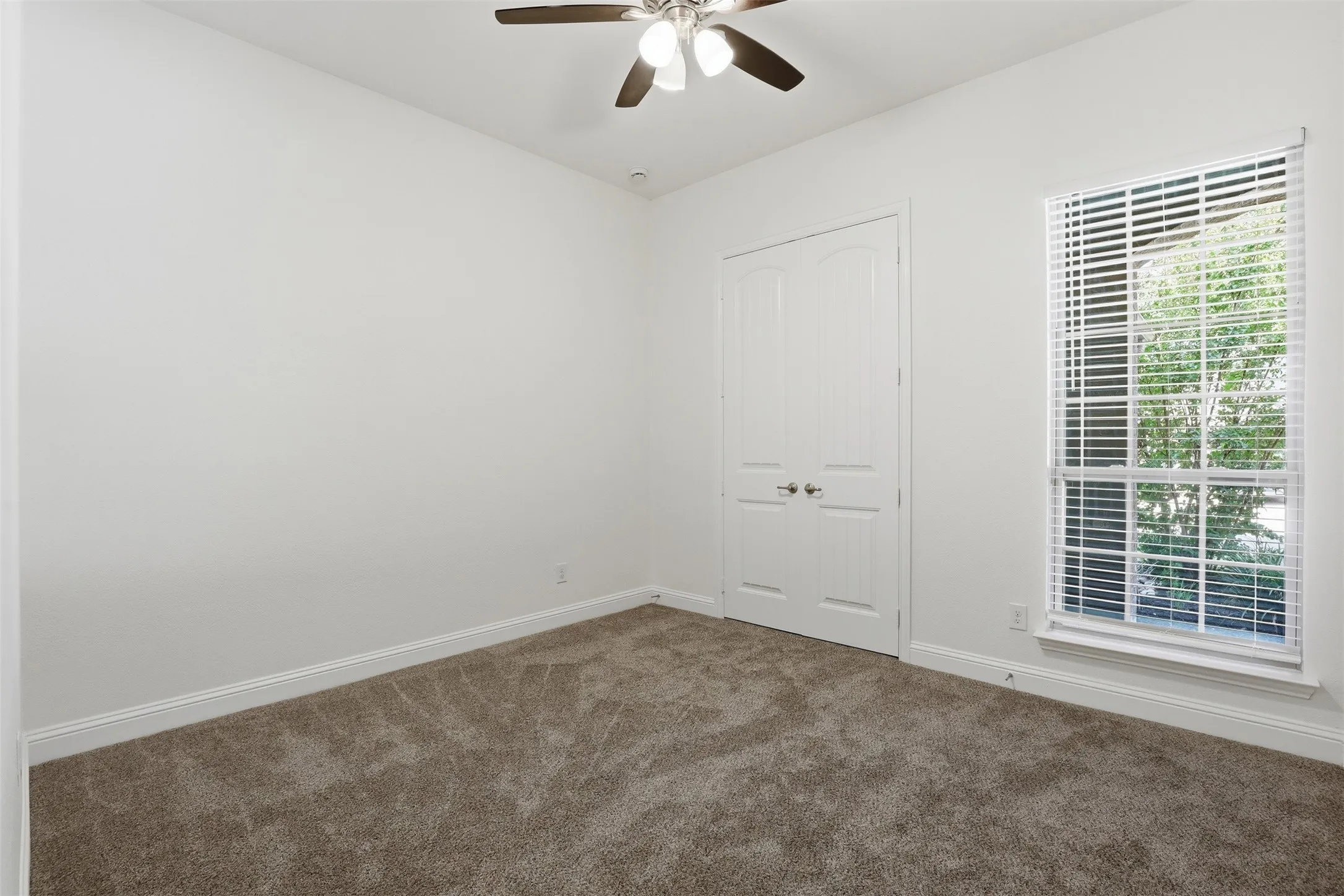 Carpeted room featuring a ceiling fan with integrated lighting, a double-door closet, a window with blinds, and white trim throughout
