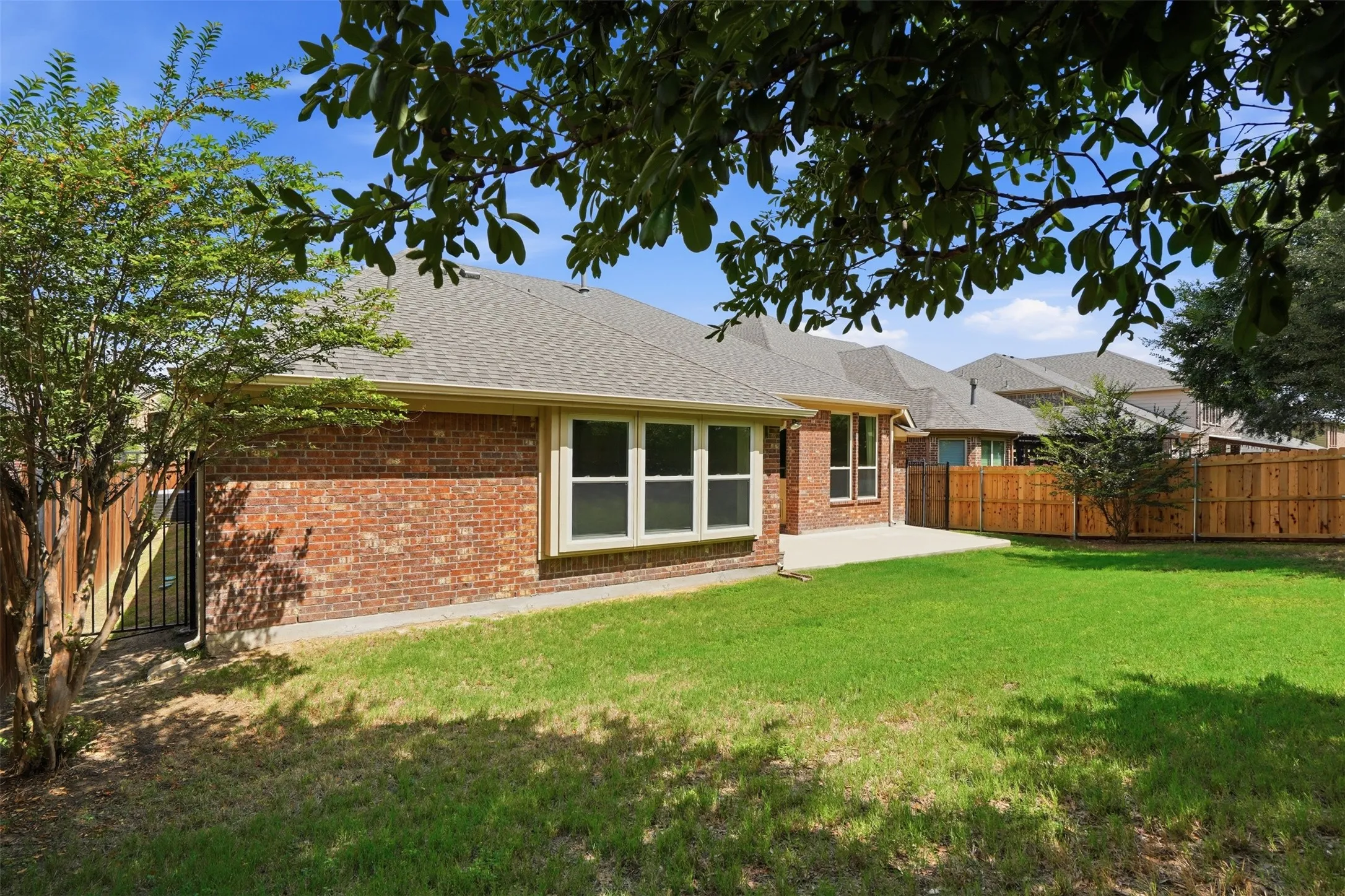 Expansive backyard featuring a manicured lawn, a large concrete patio, a full privacy fence, a brick exterior, and multiple windows