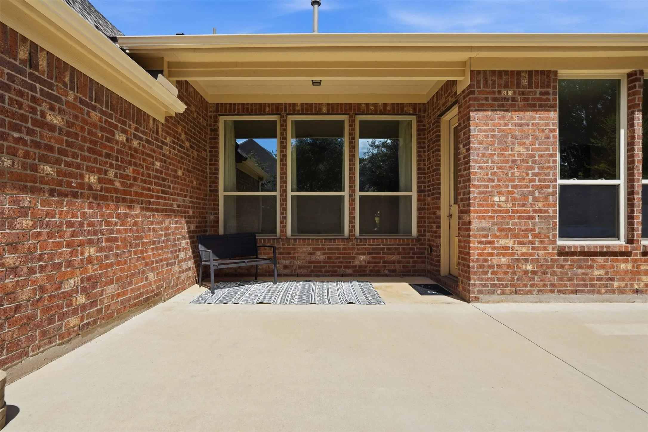 Covered patio featuring a concrete surface, brick exterior, and multiple windows