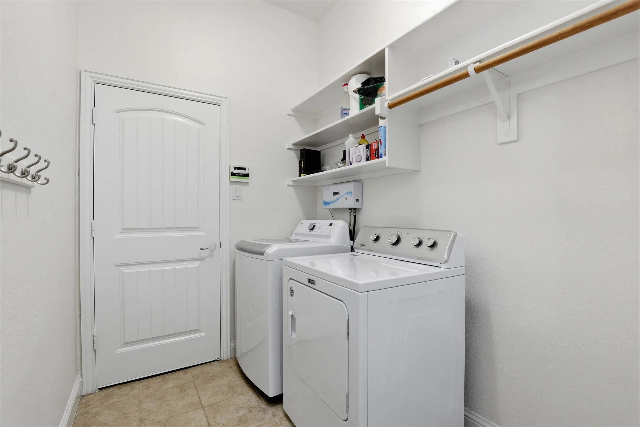 Dedicated laundry space featuring neutral-toned tile flooring, white shaker-style wall shelving, and an integrated clothing rod