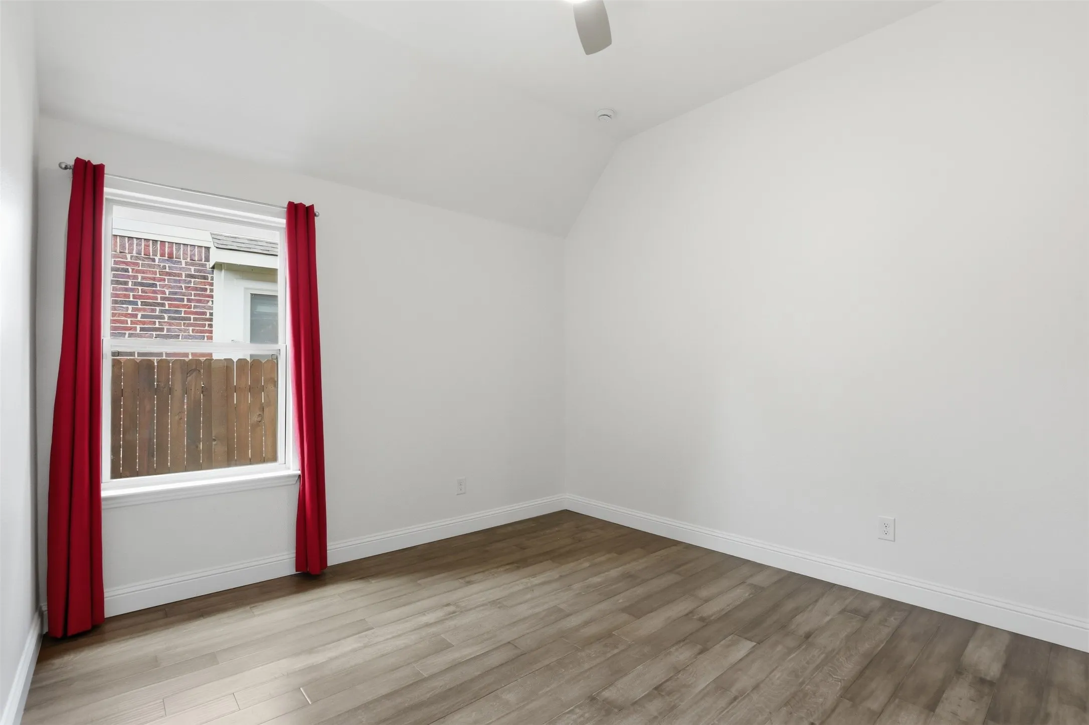 Room featuring wood-finish flooring, white baseboards, a single window, and a vaulted ceiling with a ceiling fan