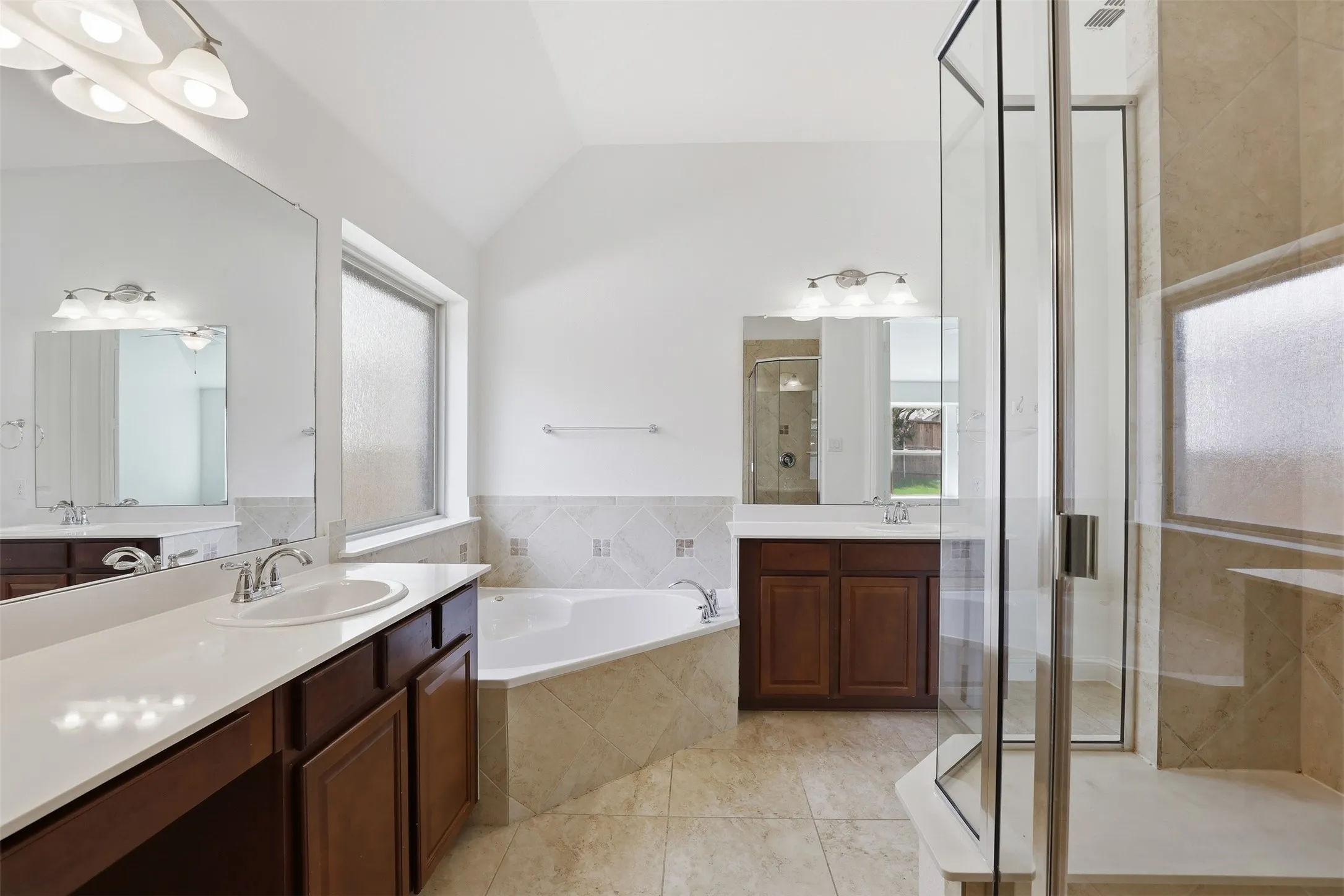 Bathroom featuring a corner soaking tub, separate glass-enclosed shower, dual vanities with integrated sinks, and tiled flooring