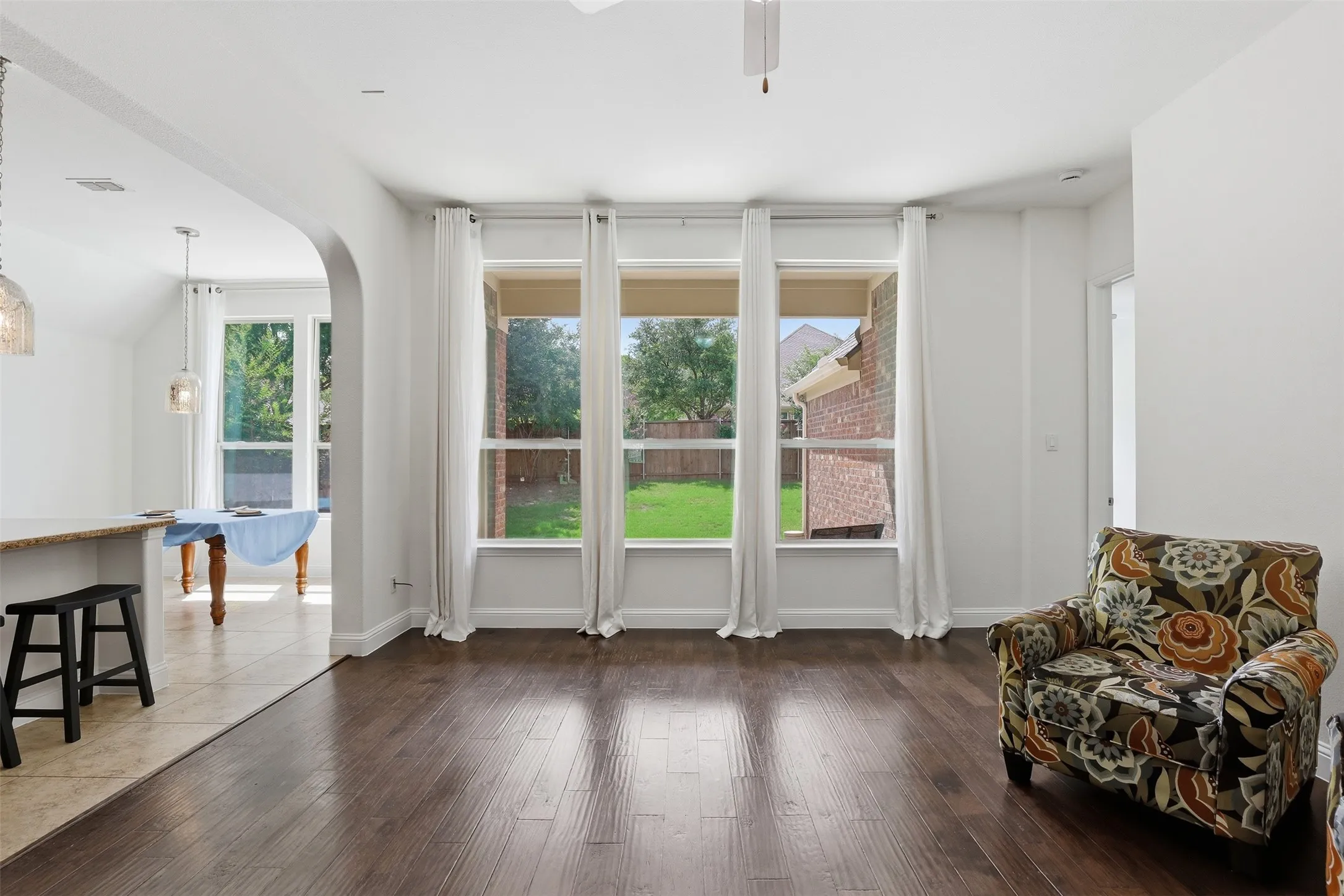 Expansive open-concept living area featuring wood-finish flooring, a wall of three large windows, and an arched entryway to the kitchen