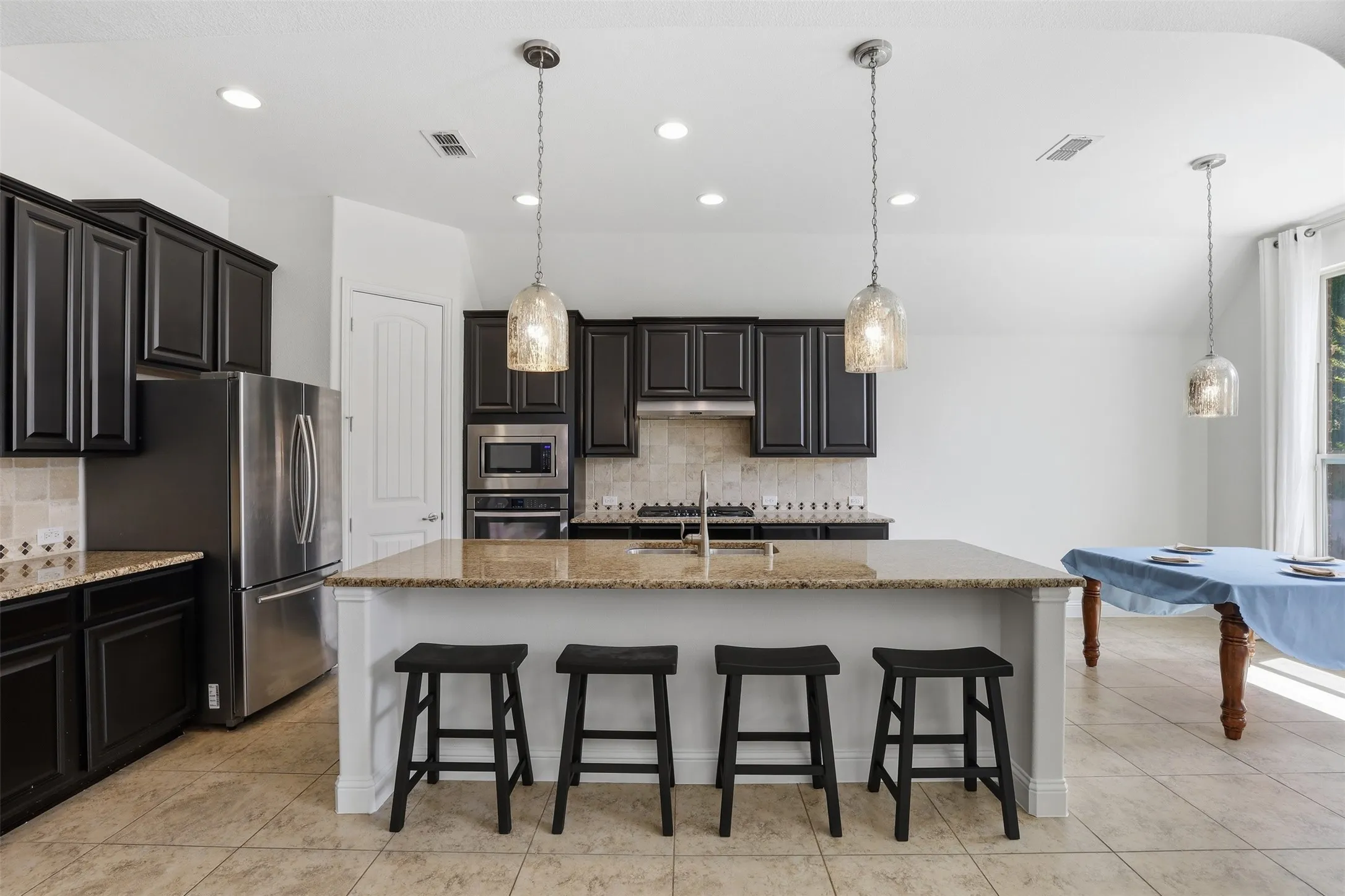 Kitchen featuring a spacious island with a granite-style countertop, dark cabinetry, stainless steel appliances, and recessed lighting