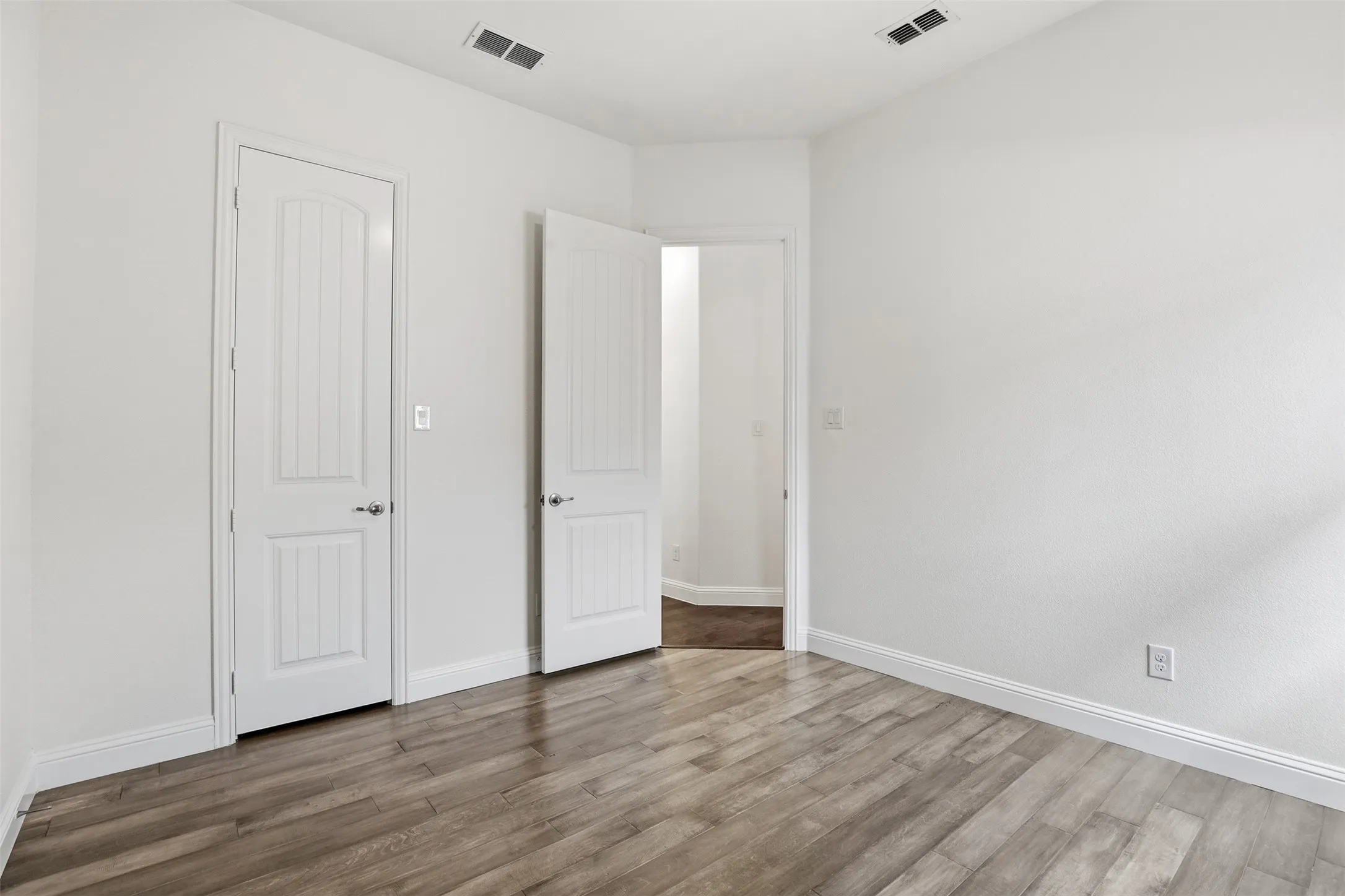 Bright interior room featuring gray wood-finish flooring, white baseboards, and white walls