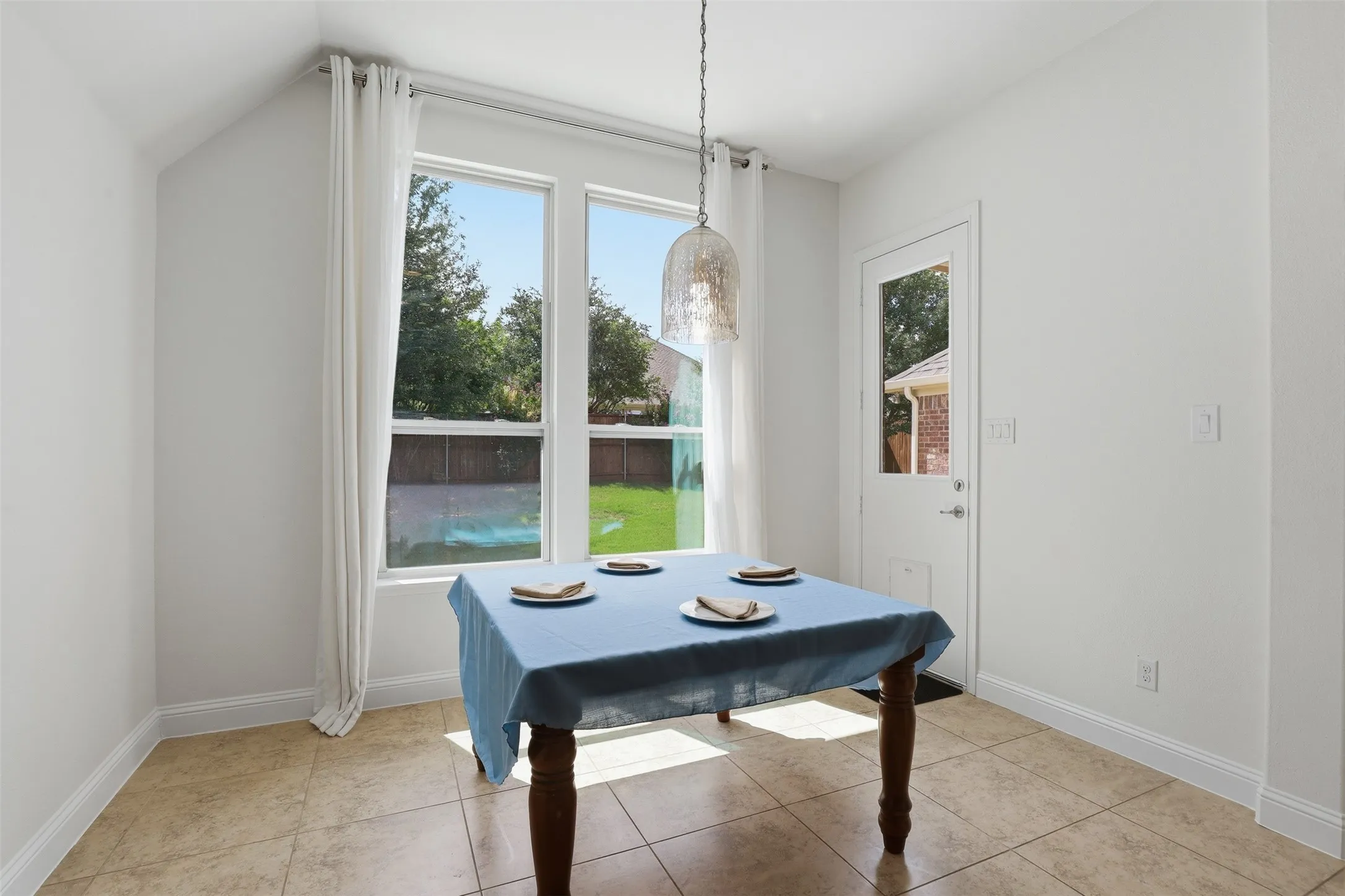 Kitchen dining area featuring large windows, a single glass-paneled exterior door, a pendant light fixture, and tile flooring