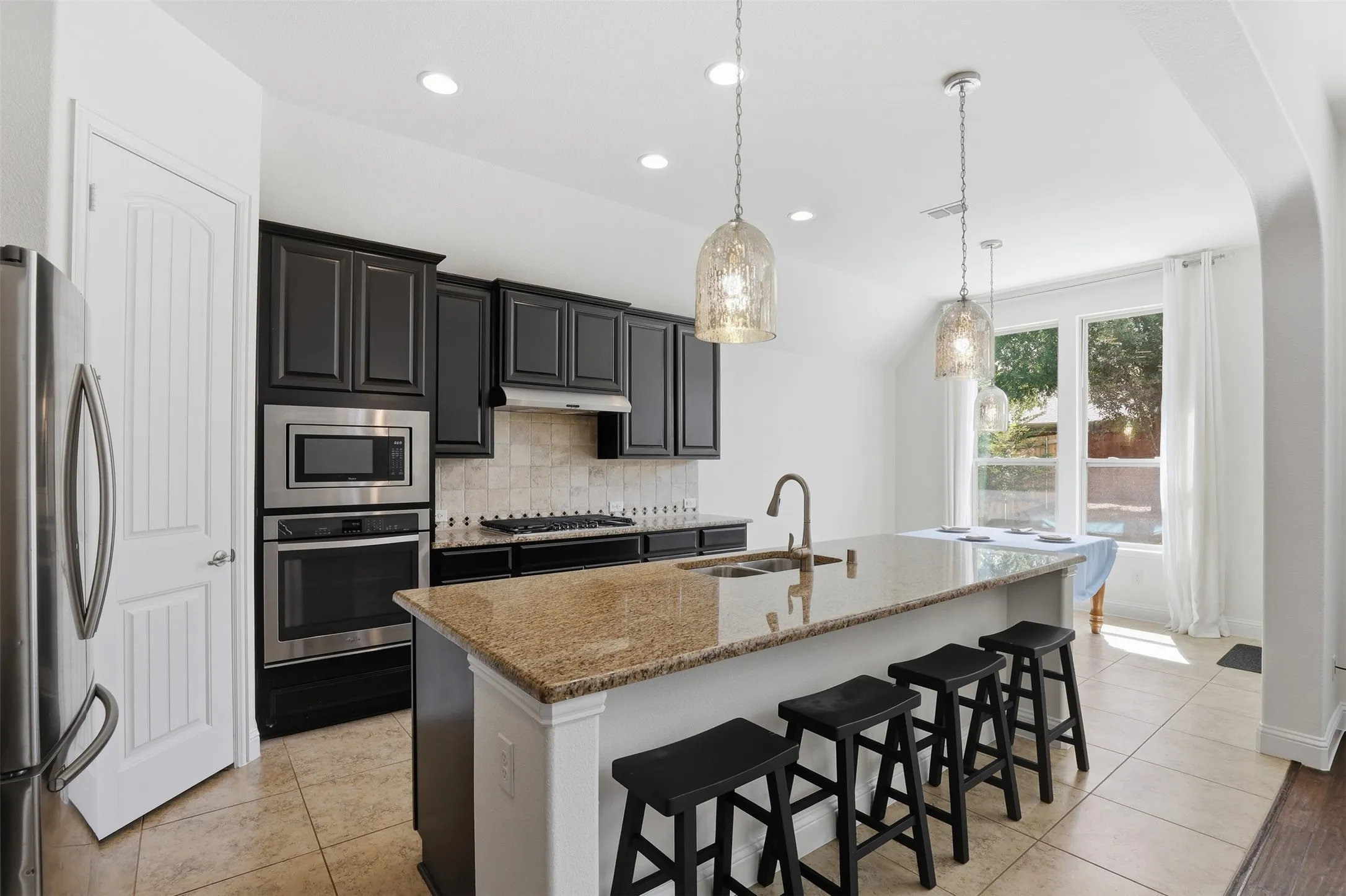 Kitchen featuring a large island with a stone countertop, dark cabinetry, stainless steel appliances, recessed lighting, and pendant light fixtures