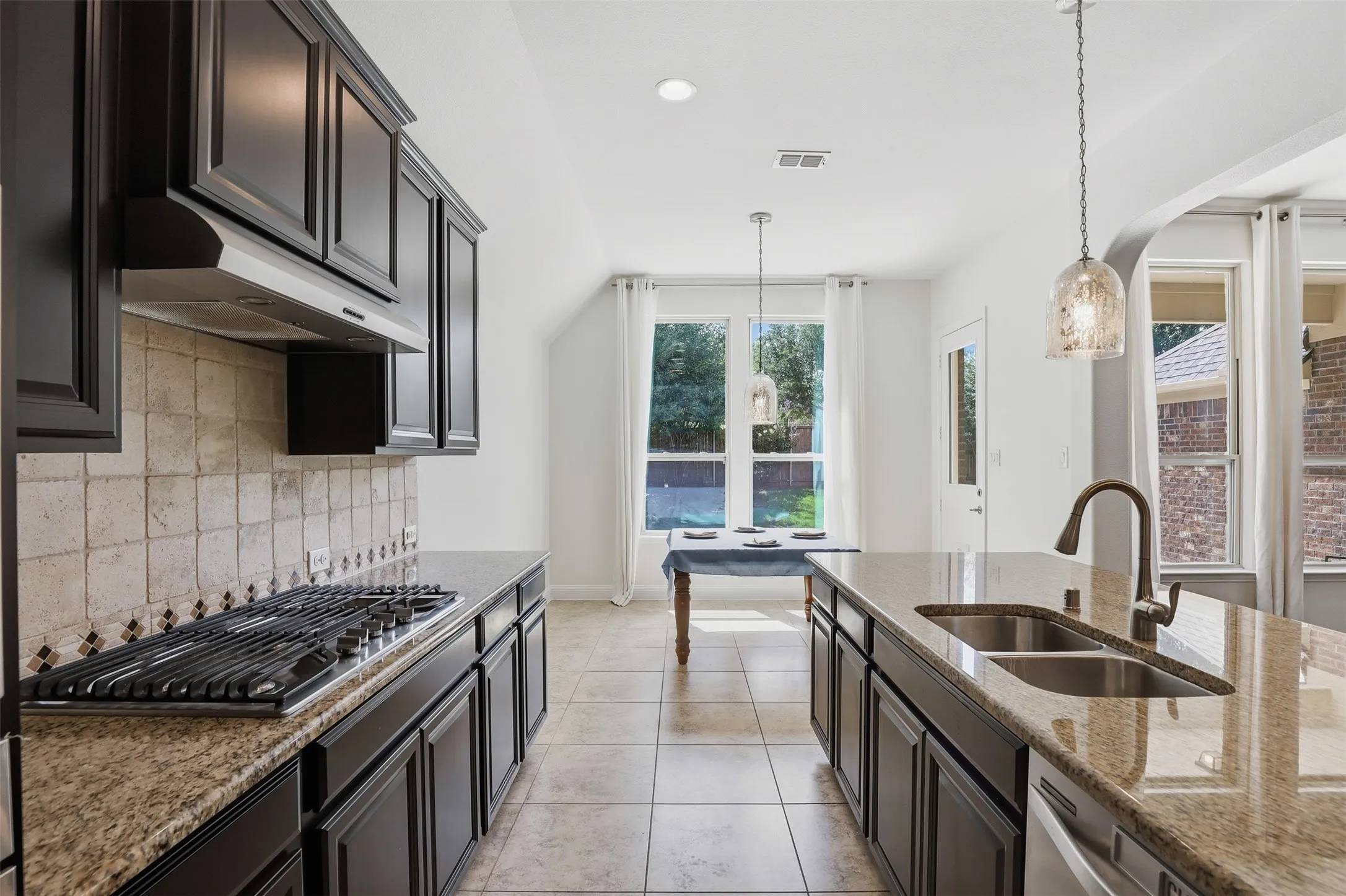 Kitchen featuring dark wood-finish cabinetry, light-toned tile backsplash, and a gas range
