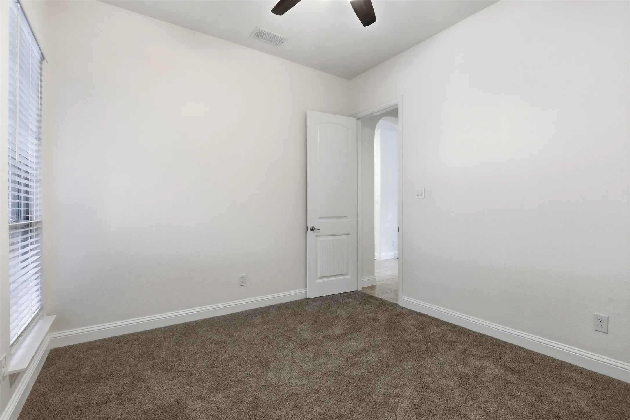 Carpeted room featuring a white interior door, a window with blinds, white baseboards, and a ceiling fan