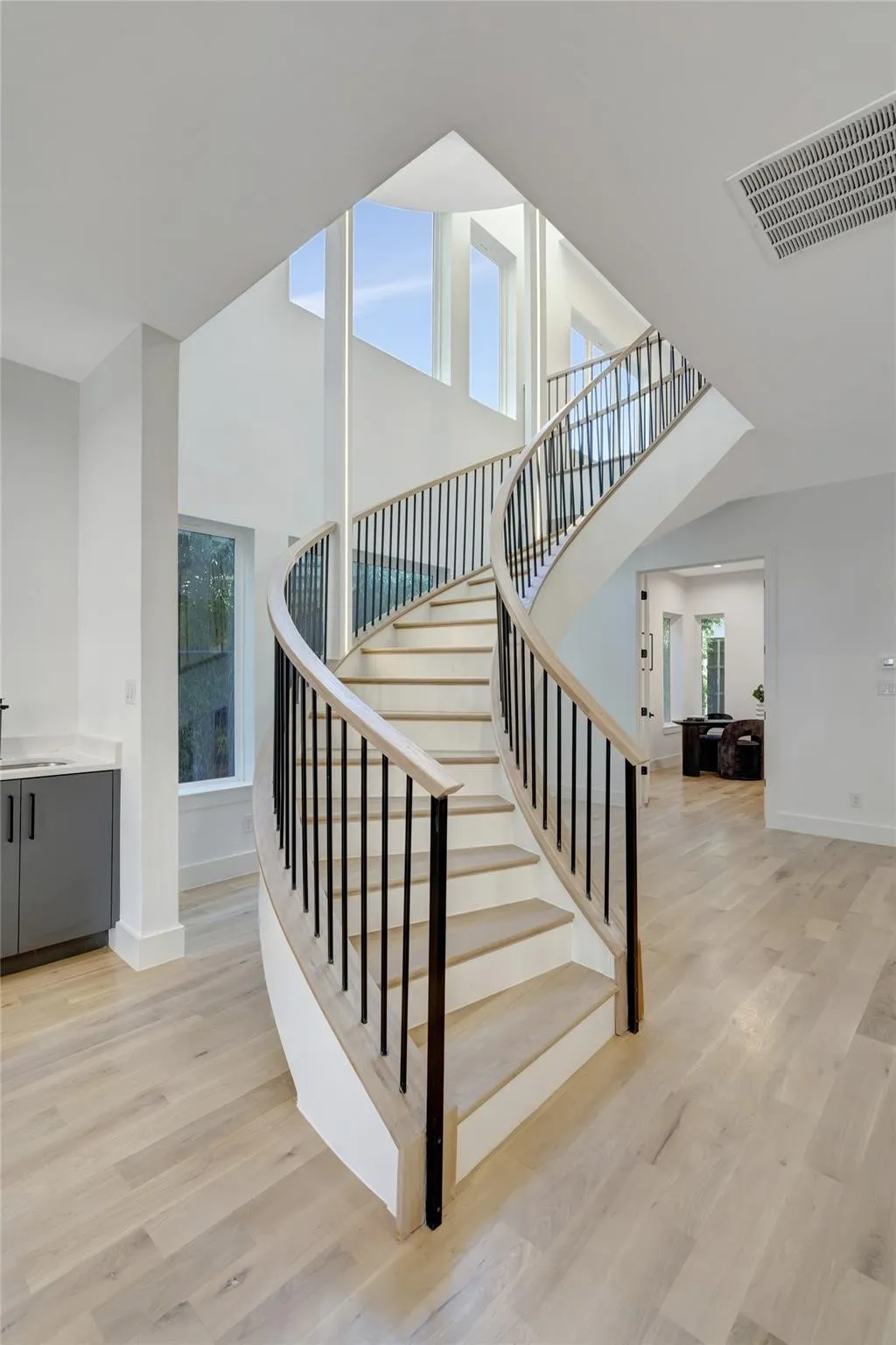 Curved staircase featuring wood-finish treads and risers, black metal balusters, and a light wood-finish handrail