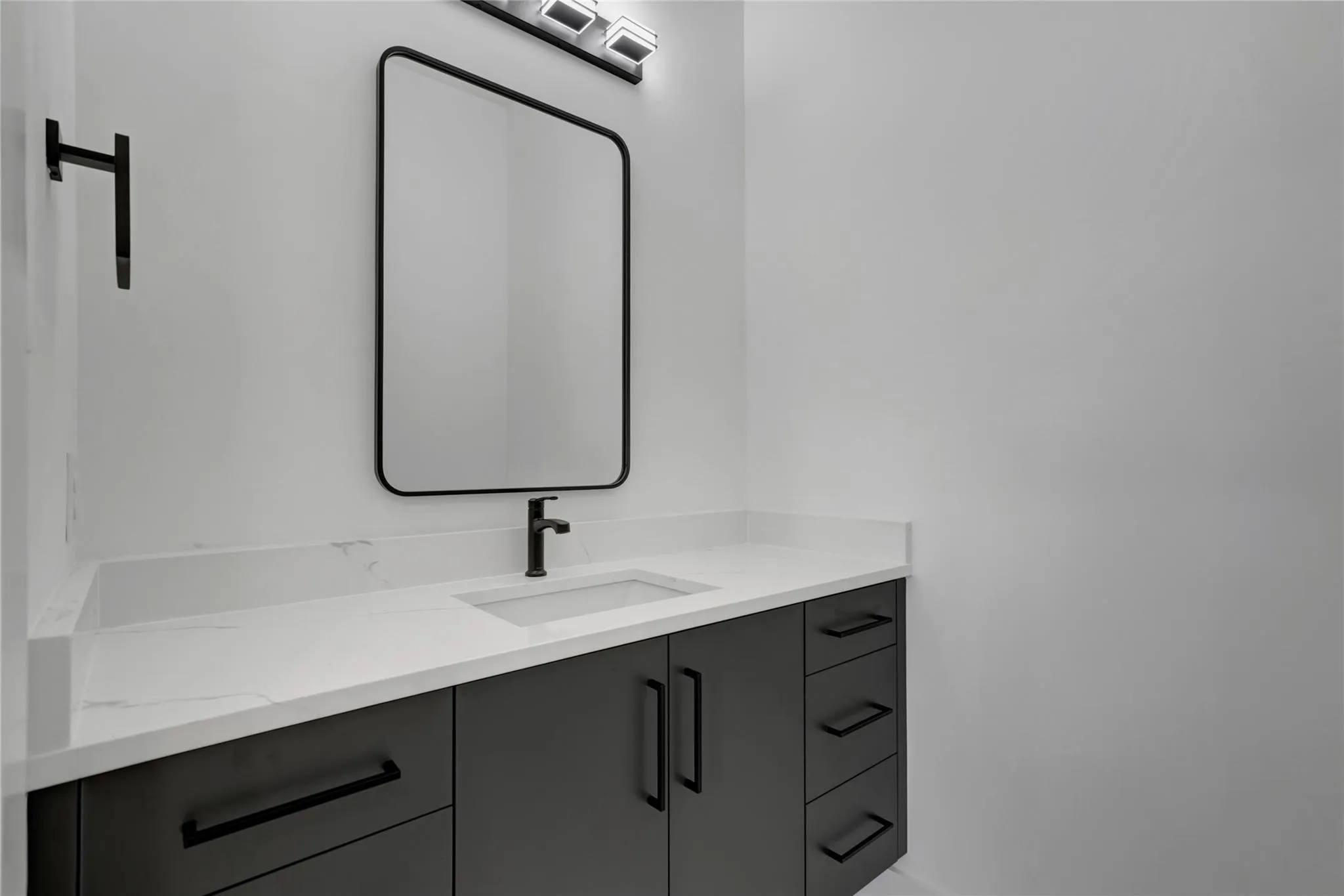 Modern vanity featuring a white countertop with integrated rectangular sink and matte black single-handle faucet