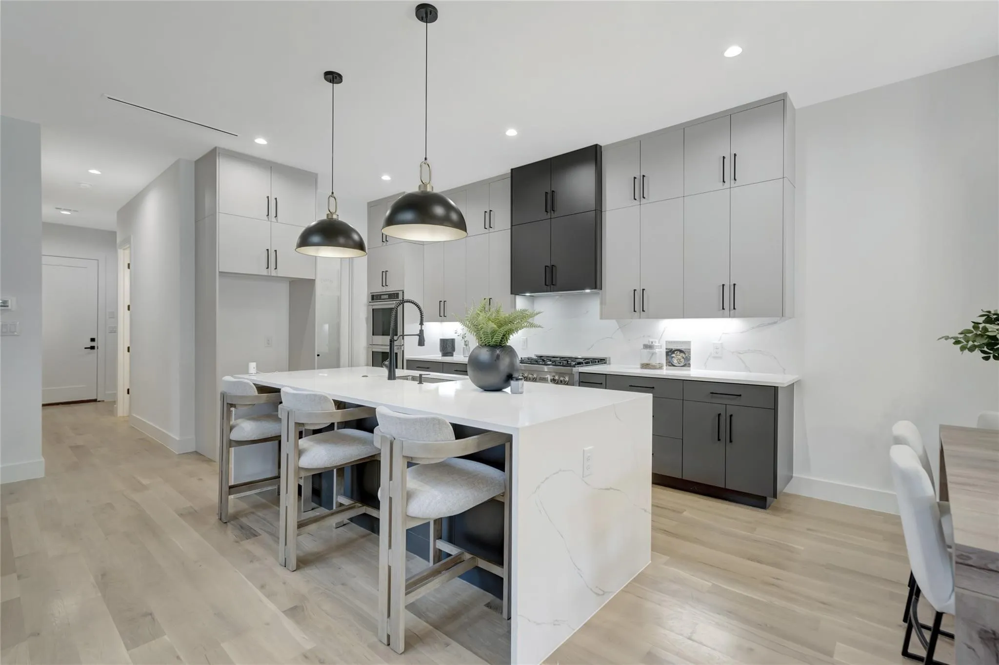 Modern kitchen featuring a waterfall island with a white quartz countertop, light wood-finish flooring, and two-tone cabinetry with matte black hardware