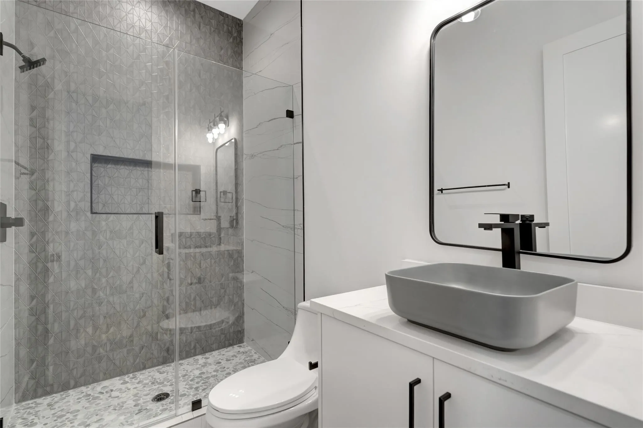 Bathroom with a glass-enclosed shower featuring textured wall tile, a built-in shower niche, and a pebble-style floor