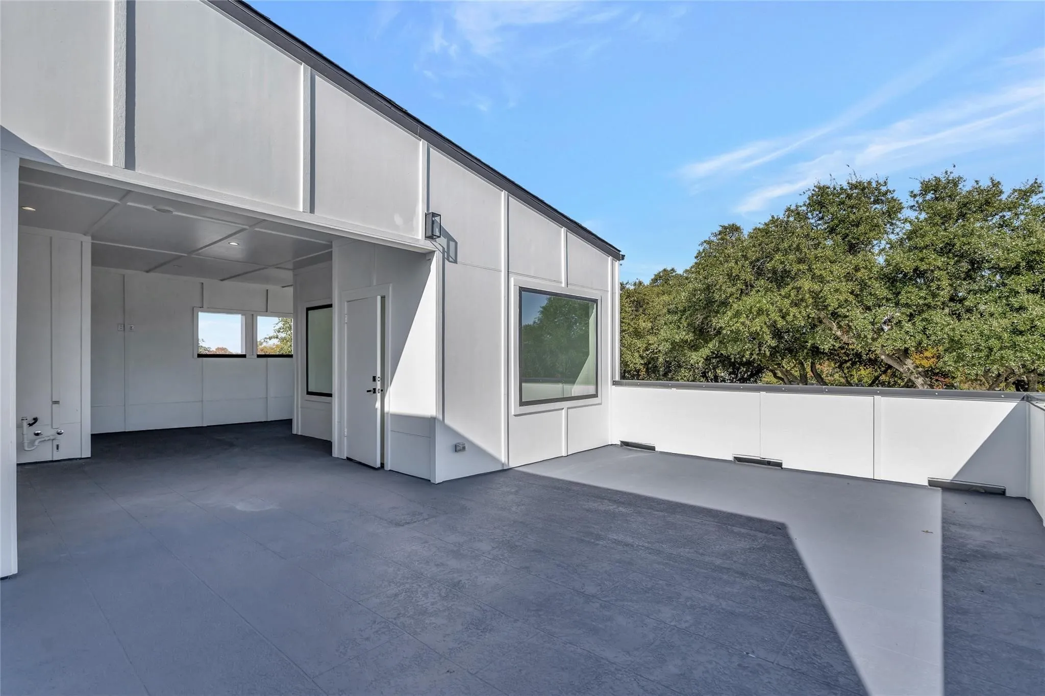 Expansive outdoor patio featuring a durable dark gray surface, white exterior siding, and a partial outdoor room with recessed lighting