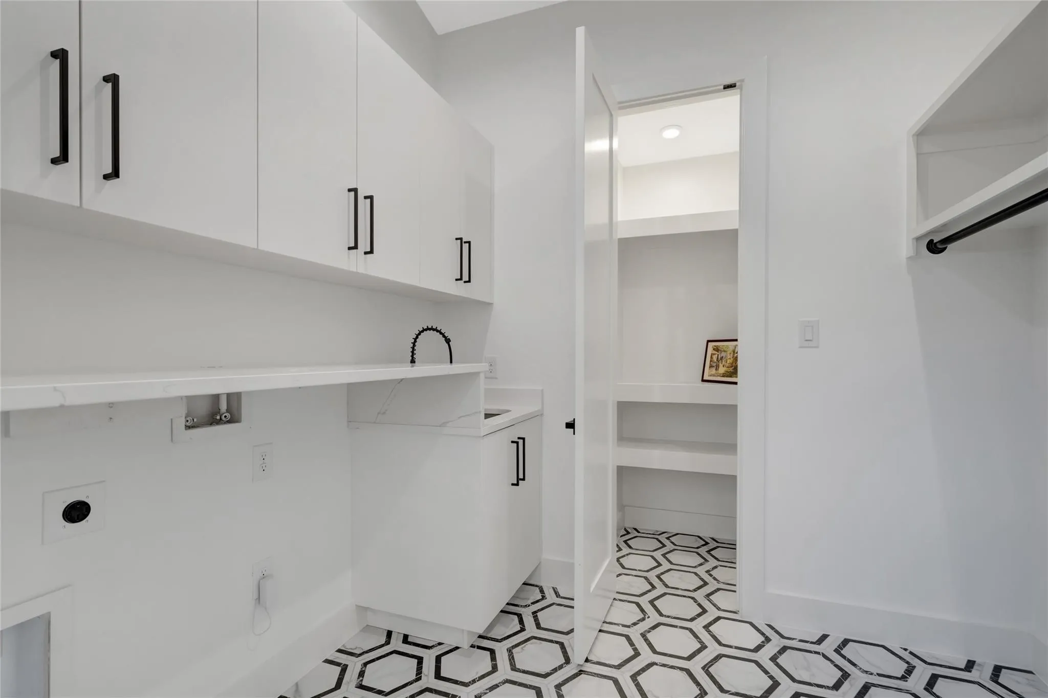Utility space featuring white cabinetry with black hardware, a built-in countertop, and a utility sink
