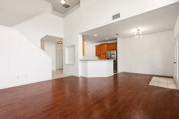 Spacious open-concept interior featuring high ceilings, rich wood-finish flooring, and a kitchen with warm-toned cabinetry and a breakfast bar