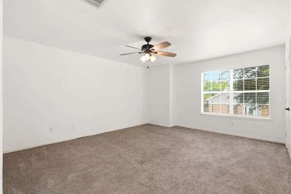 Spacious room featuring neutral carpet, white walls, a large window with blinds, a ceiling fan with light fixture, and an air conditioning vent