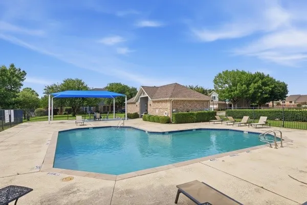 Community swimming pool featuring a concrete deck and blue shade structure