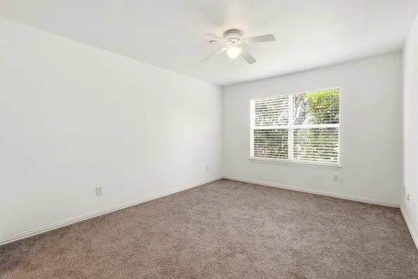 Neutral-toned carpeted room with white walls and a white ceiling fan with integrated lighting