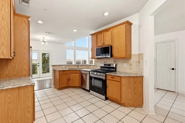 Kitchen featuring light wood cabinetry, granite-finish countertops, tile backsplash, stainless steel appliances, and a gas range