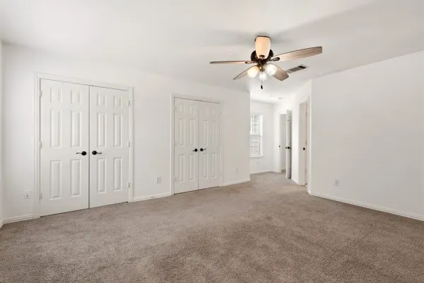 Spacious room featuring neutral carpeting, a ceiling fan with integrated lighting, multiple paneled doors with dark hardware, white baseboards, and bright white walls
