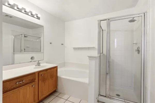 Bathroom featuring a glass-enclosed shower, a built-in tub, a vanity with wood-finish cabinetry, a single basin sink, and a large mirror with overhead lighting