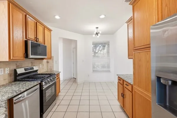 Kitchen featuring wood cabinetry, granite-style countertops, stainless steel appliances, and a tiled backsplash