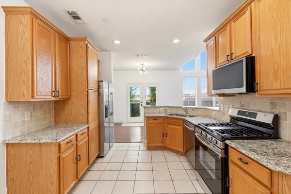 Kitchen featuring wood cabinetry, granite-finish countertops, tile backsplash, stainless steel appliances, and tile flooring